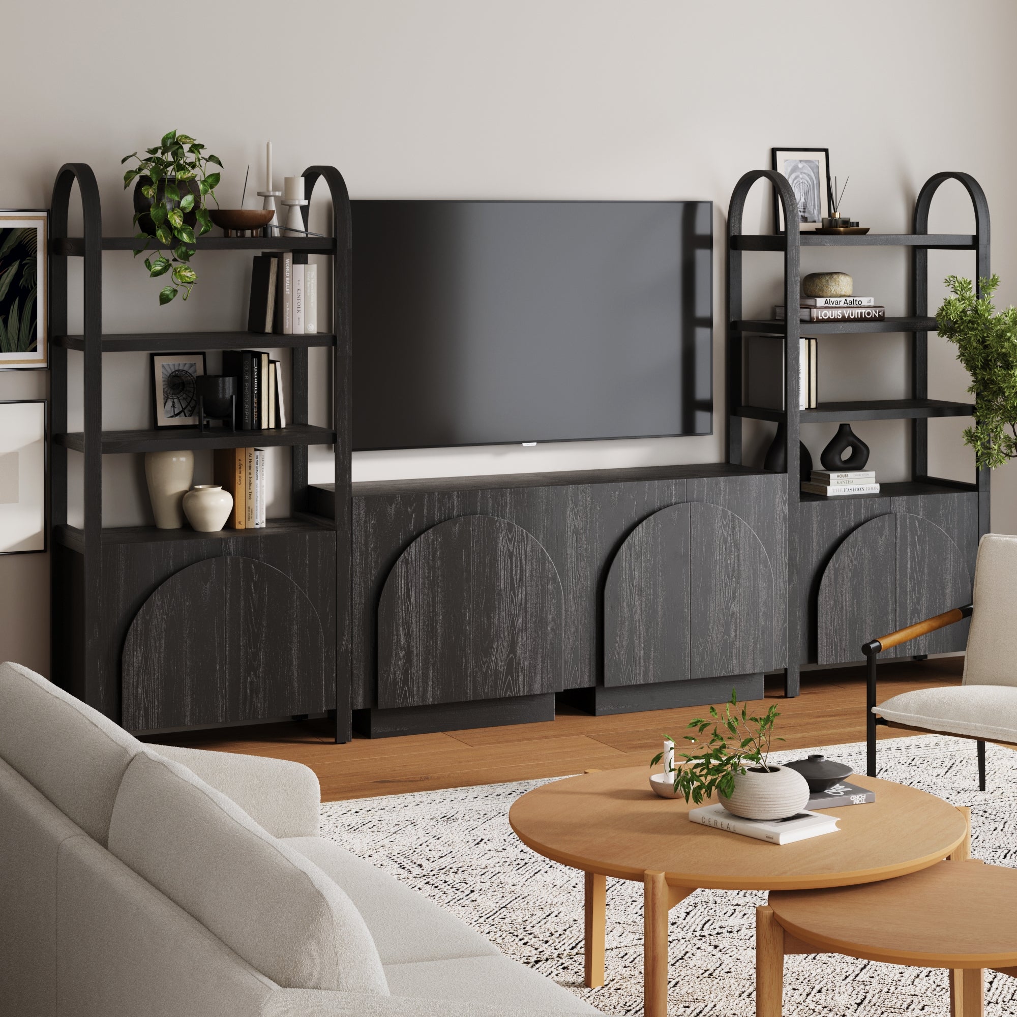 A modern living room features the Nathan James Mid-Century Entertainment Center Black (2 Cabinets) with open shelves, a flat-screen TV, plants, books, and décor, paired with a beige sofa, round coffee table, and textured rug.
