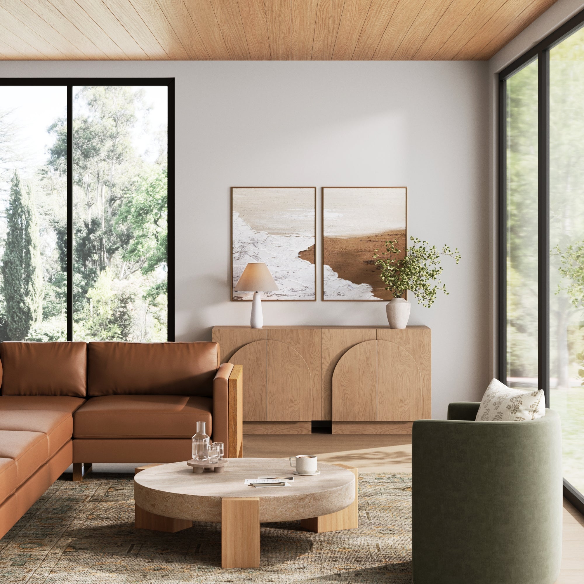 A modern living room features a brown leather sectional, round coffee table, green armchair, and the Nathan James Wood Mid-Century Arched Storage Cabinet in oak with vases. Large windows show greenery and two framed beach-themed artworks hang on the wall.