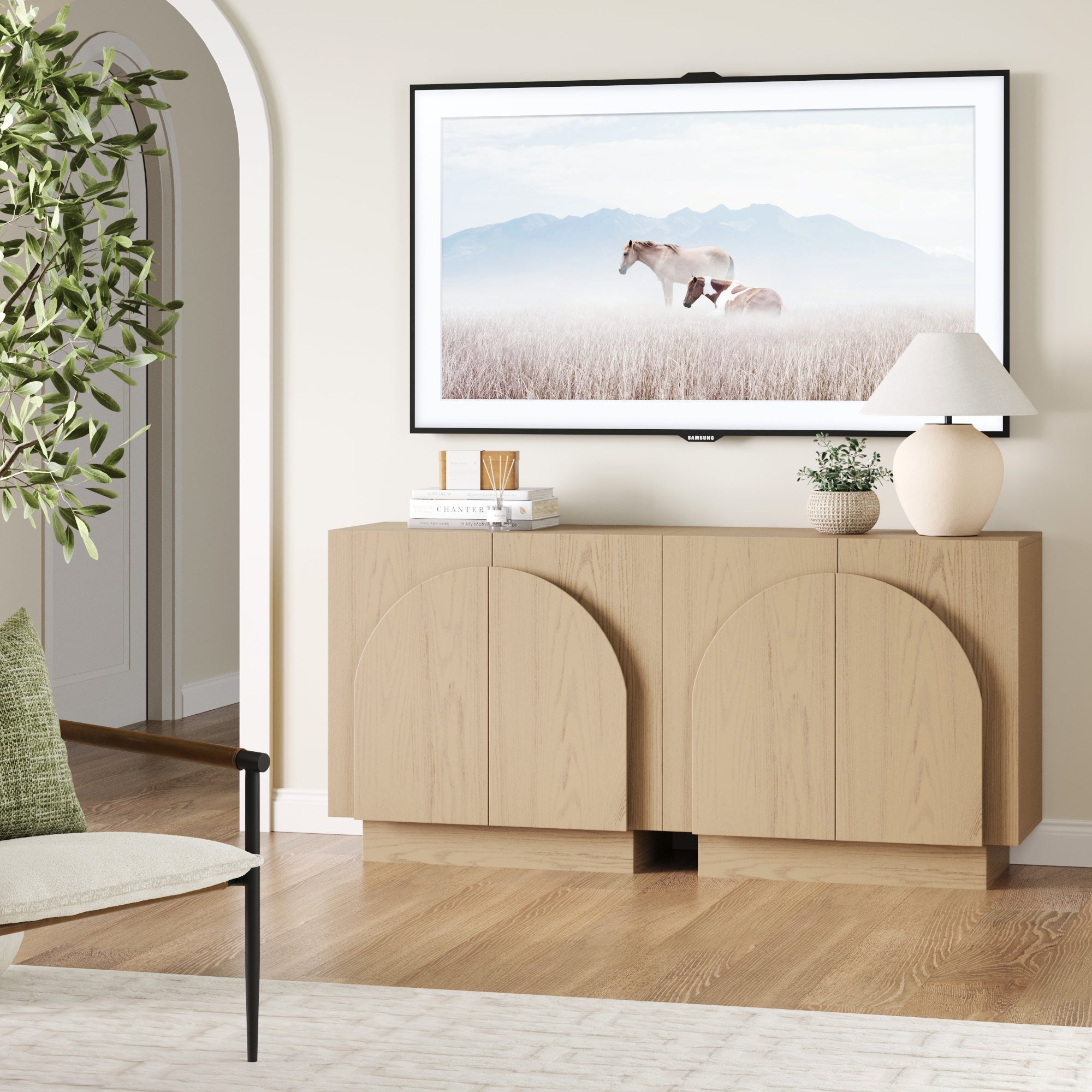 The Nathan James Wood Mid-Century Arched Storage Cabinet in Gray Oak (Set of 2) stands against the wall, topped with a lamp, plant, and decor. Above, a framed horse photo hangs. A nearby chair and plant complete the scene.