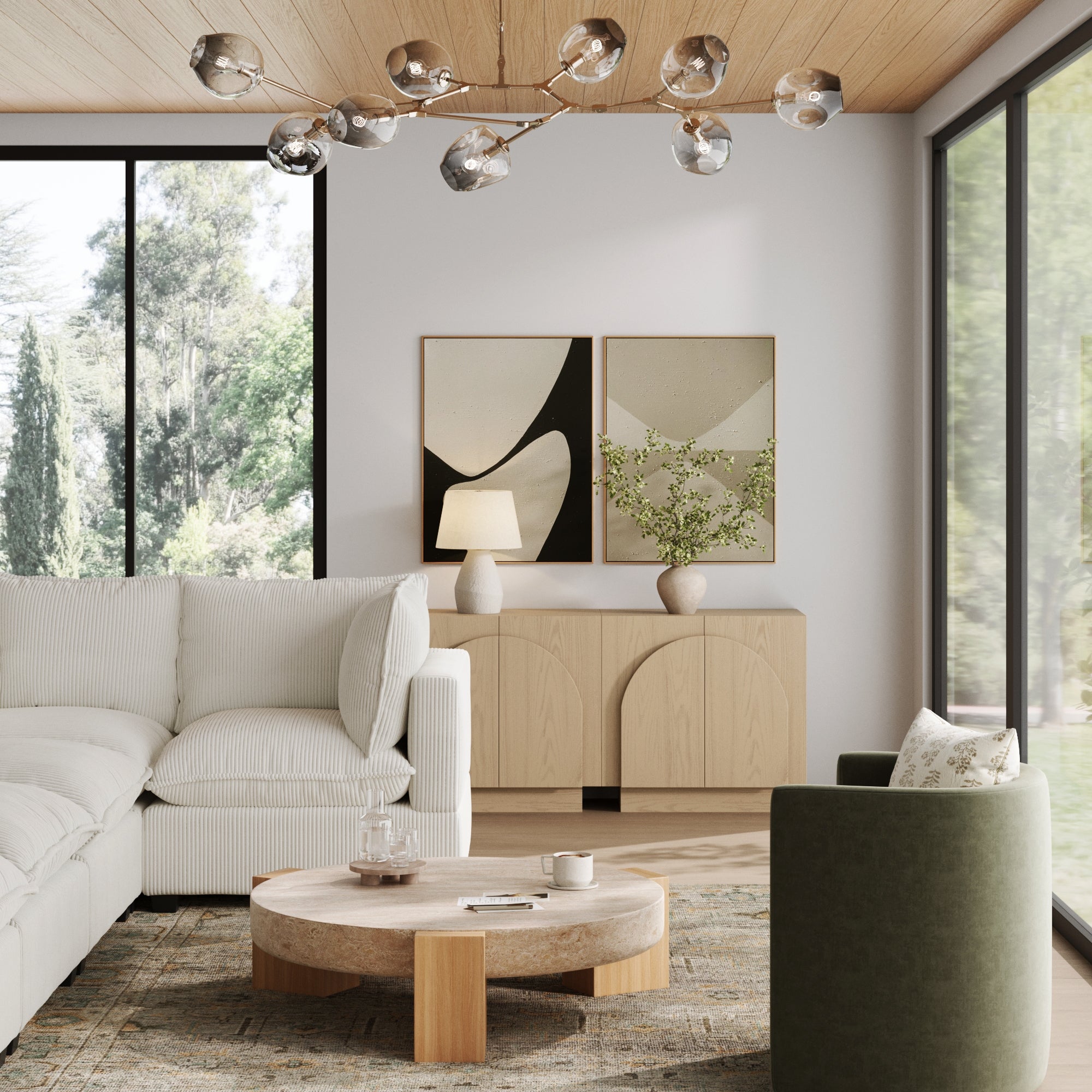 A modern living room with large windows, a white sectional sofa, a round stone coffee table, a green armchair, abstract wall art, a branch chandelier, and the Nathan James Wood Mid-Century Arched Storage Cabinet in Gray Oak.