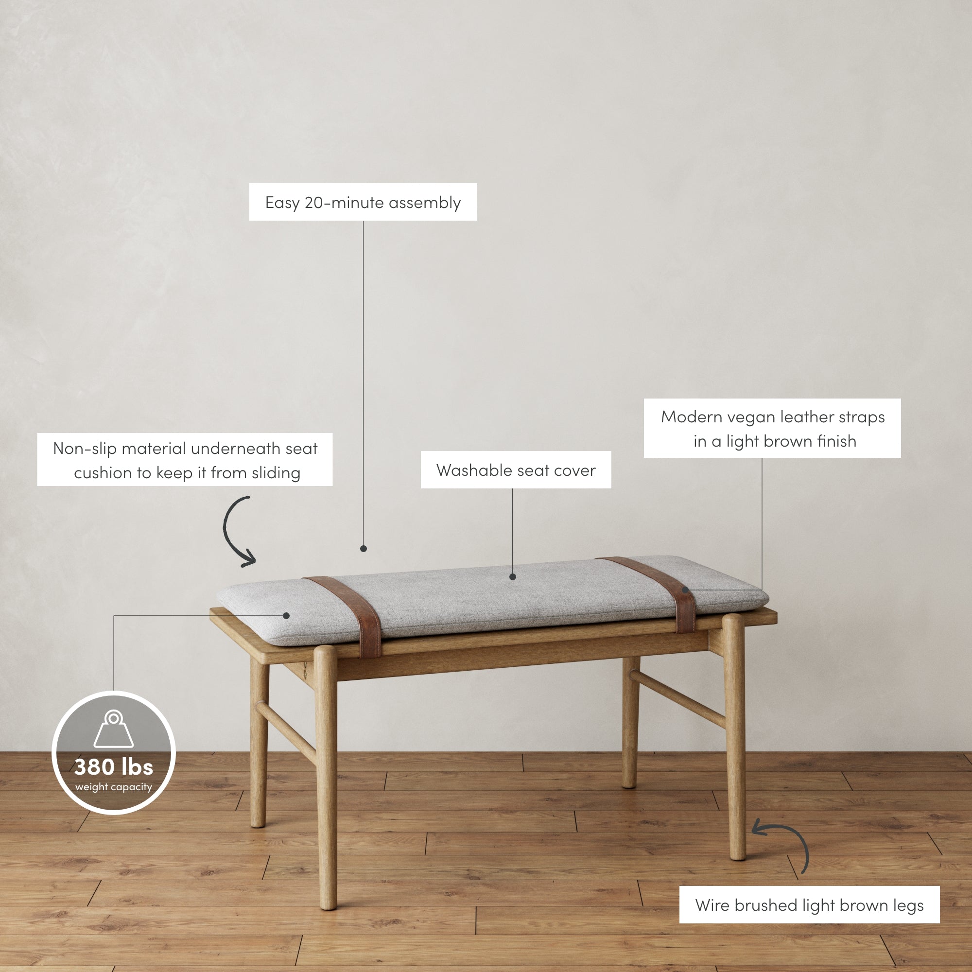 A modern bench with a light gray washable seat cover, non-slip material underneath, vegan leather straps, wire brushed light brown legs, easy 20-minute assembly, and a 380 lbs weight capacity, on a wooden floor.