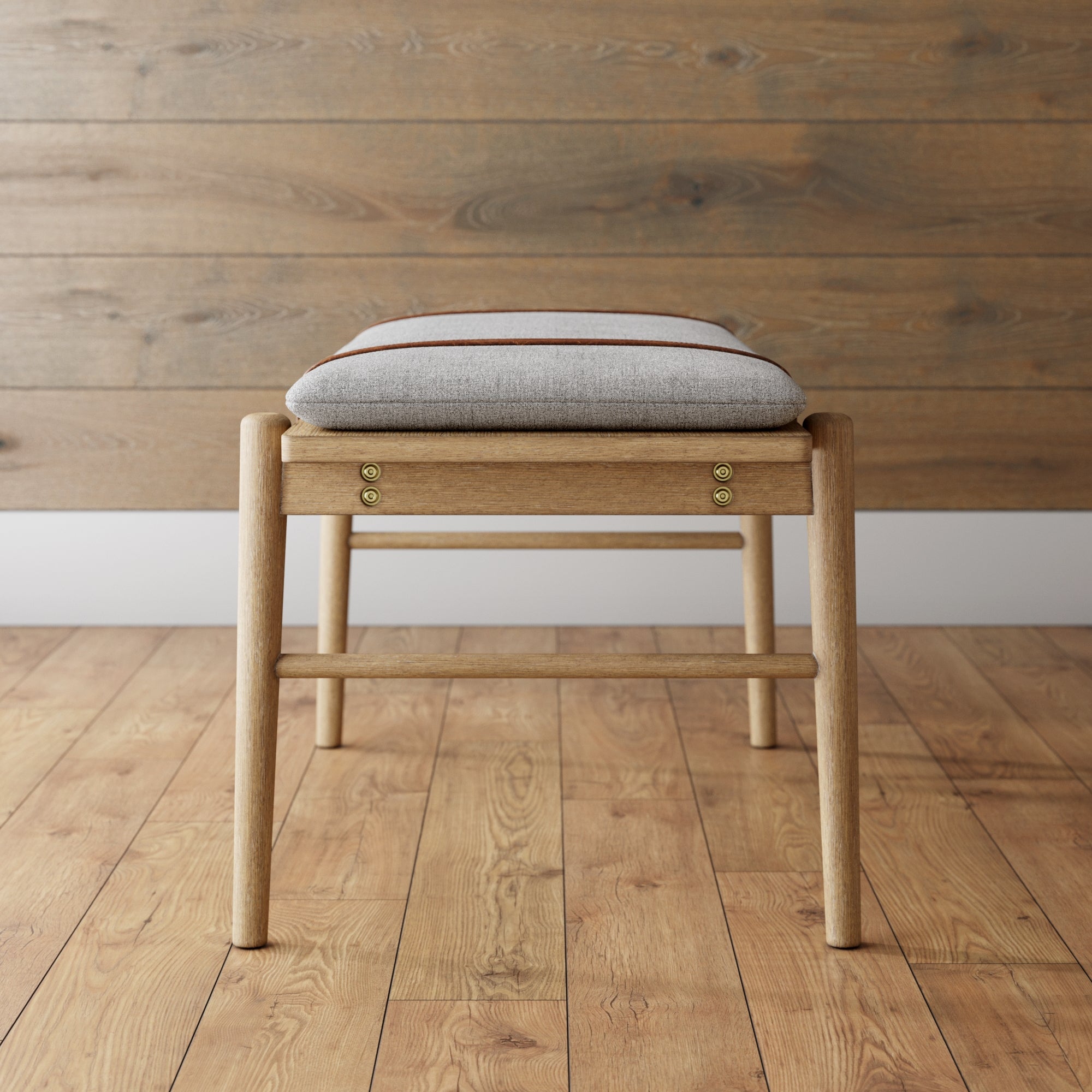 A wooden stool with a light gray cushioned seat, placed on a wood floor against a wood-paneled wall. The stool has round legs and simple, clean lines in a minimalist design.