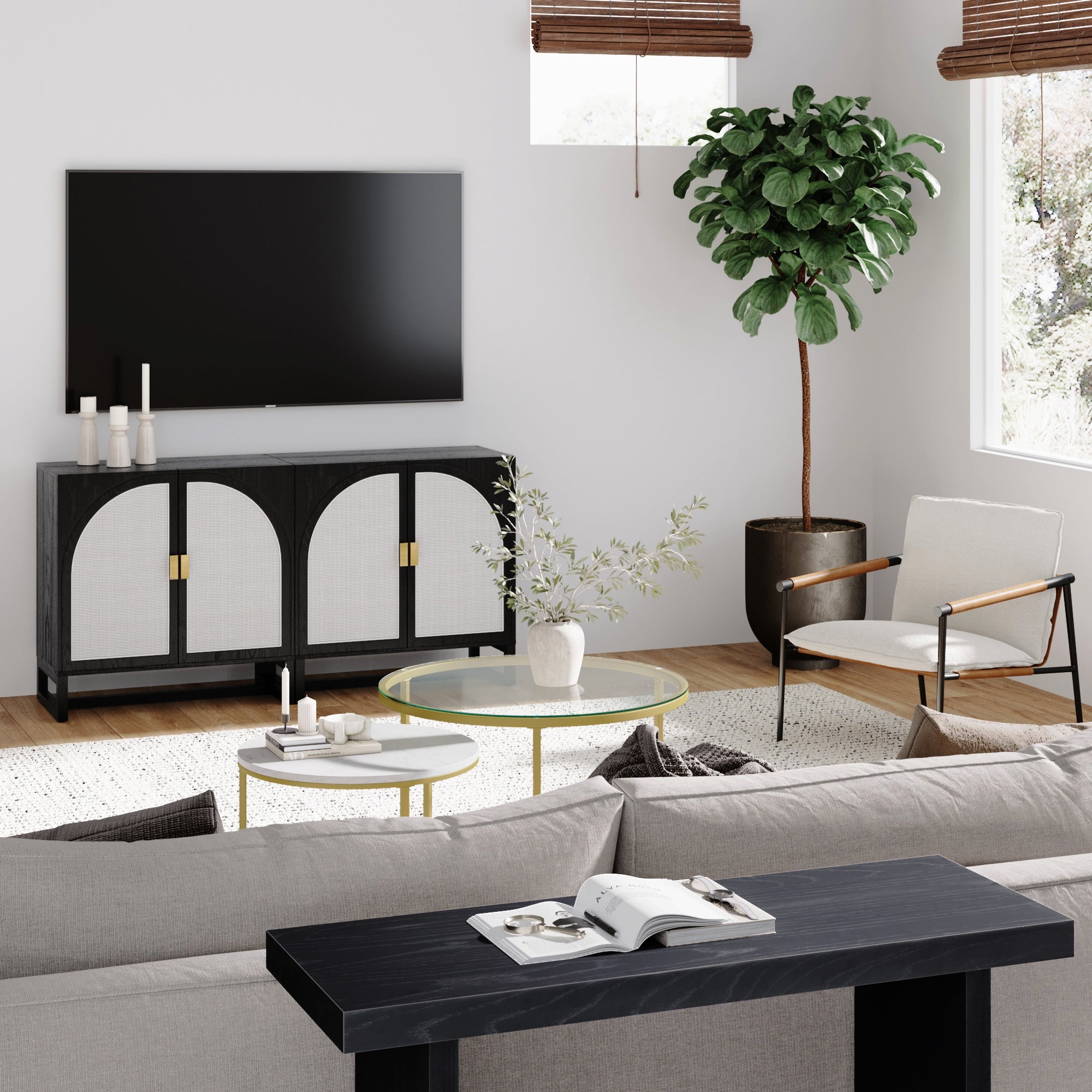 Modern living room with a wall-mounted TV, black and white cabinet, round glass coffee tables, white armchair, potted plant, and a light gray sofa on a white rug. Sunlight streams through a window with wooden blinds.