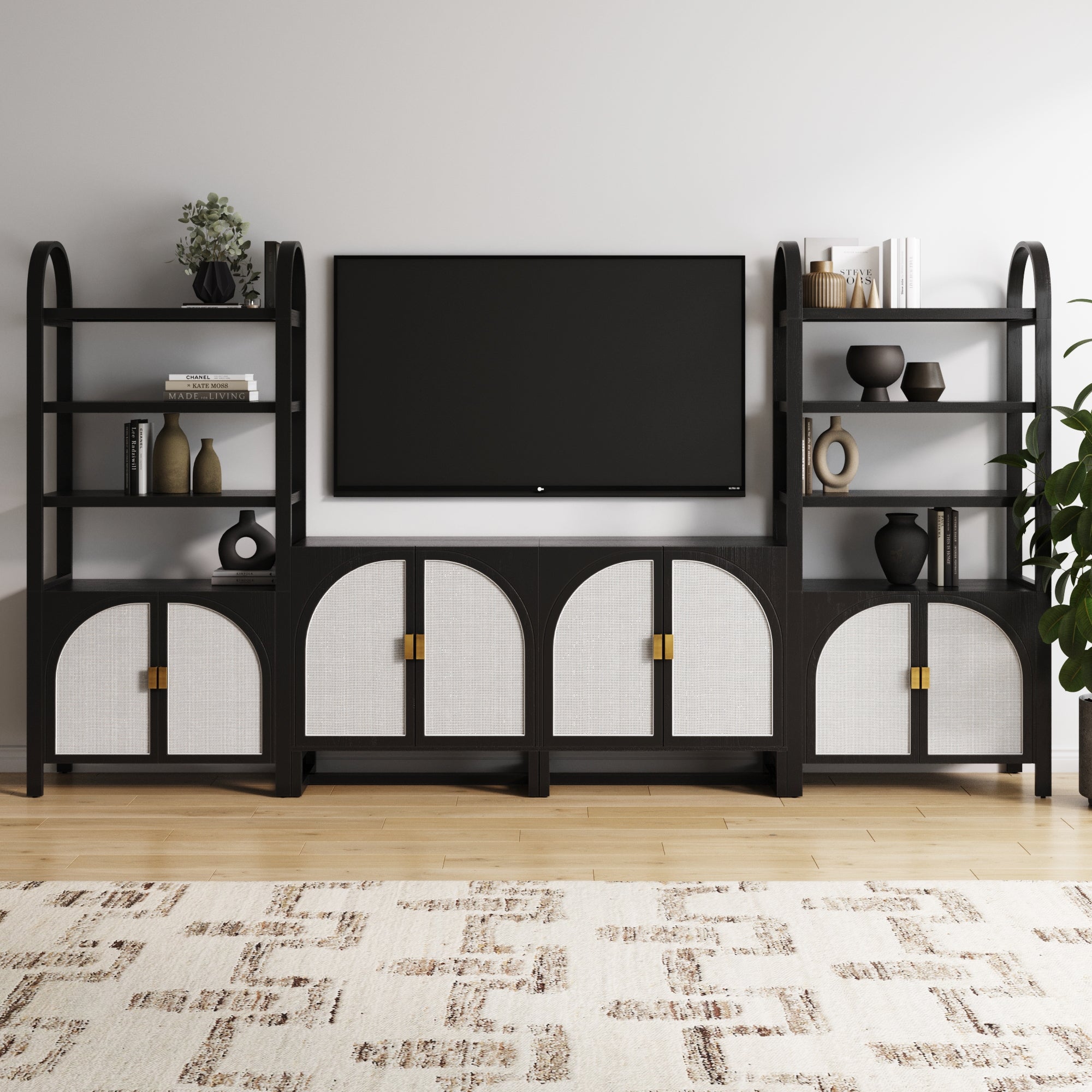 The Nathan James Boho Arched Bookshelf & Cabinet Set TV Stand in black features stylish storage and display for decor, books, and plants beside a wall-mounted TV, beautifully set against a light wall and wooden floor with a patterned rug.