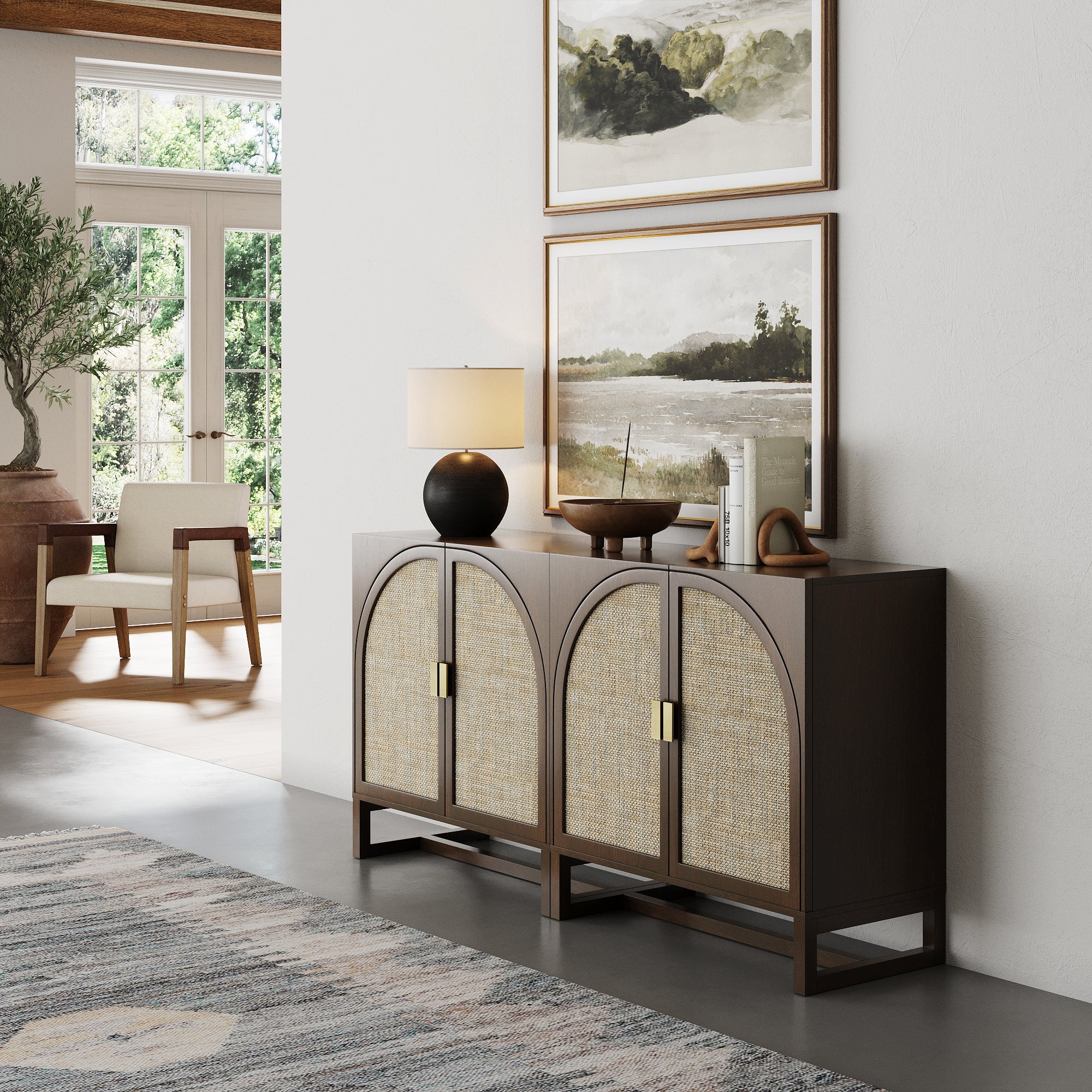 The Nathan James Boho Arched TV Console Credenza Dark Acacia (Set of 2) stands against a white wall with decor on top. Two landscape paintings hang above, while sunlight streams in through nearby tall windows.