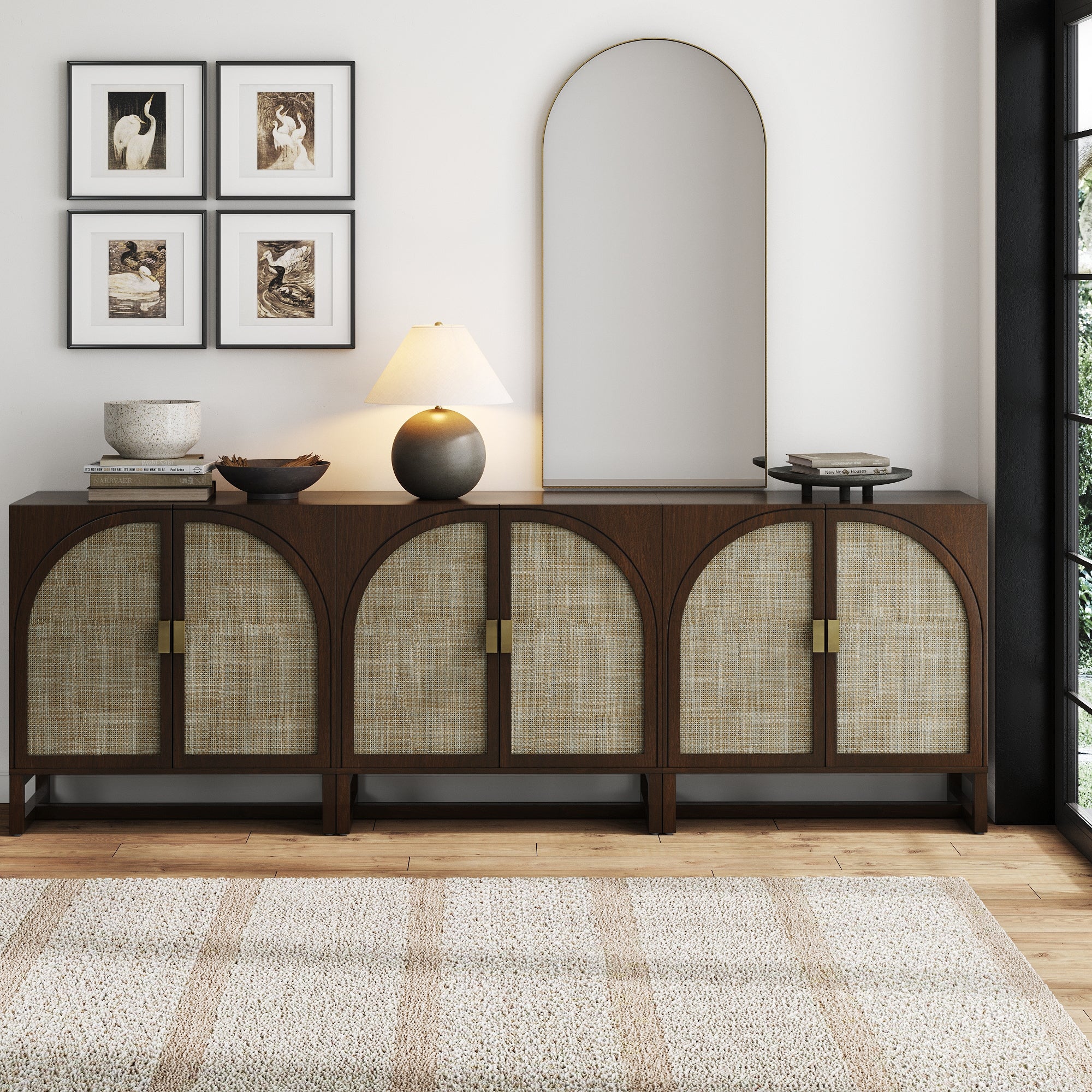 The Nathan James Boho Arched TV Console Credenza Dark Acacia (Set of 3) stands against a white wall, topped with a lamp, bowls, and decor. Above it hang four framed animal prints, paired with an arched mirror and textured rug below.