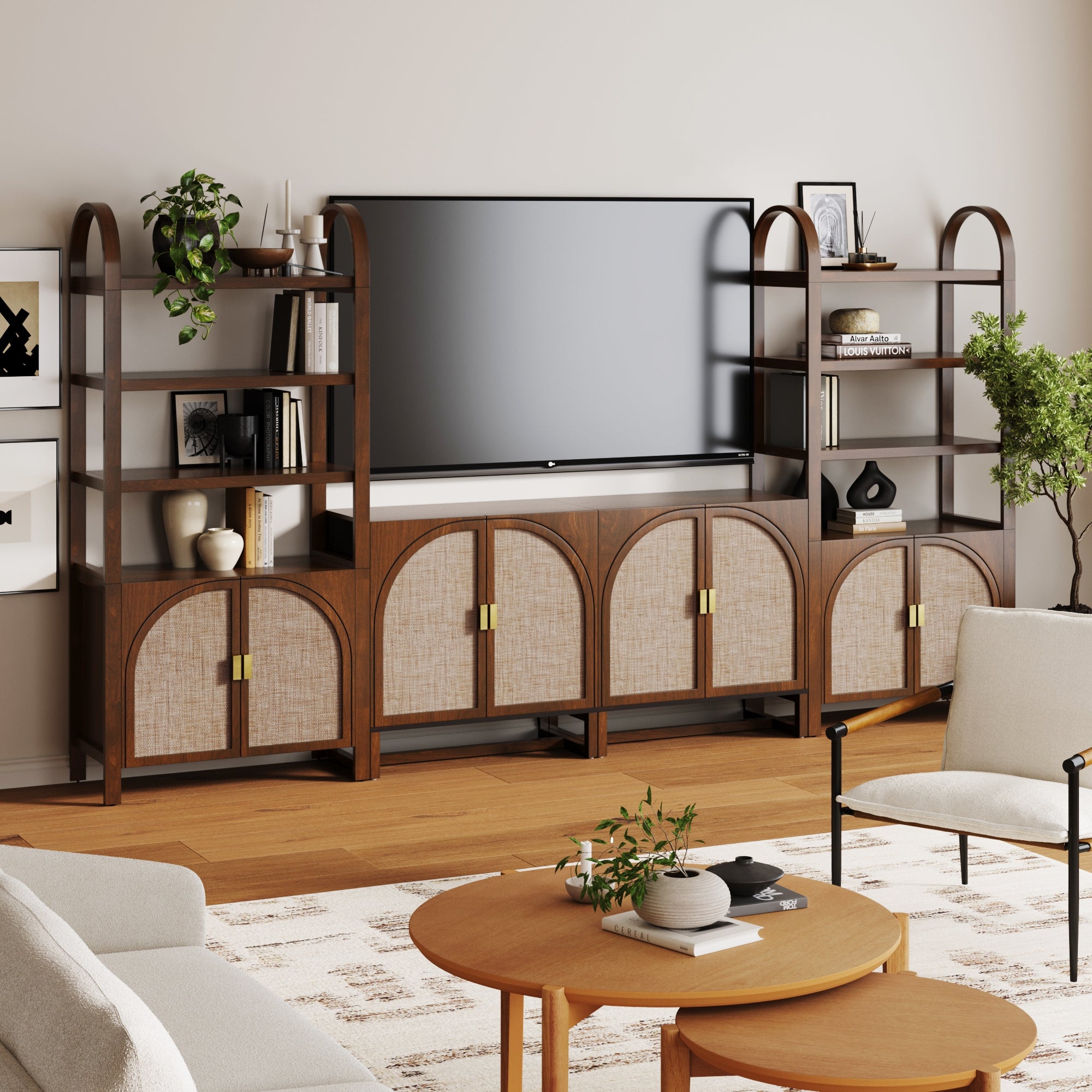 A contemporary living room showcases the Nathan James Arched Entertainment Center in dark acacia, featuring faux rattan cabinets and open shelves for plants, books, and decor. Light armchairs and a round coffee table rest on a patterned rug.