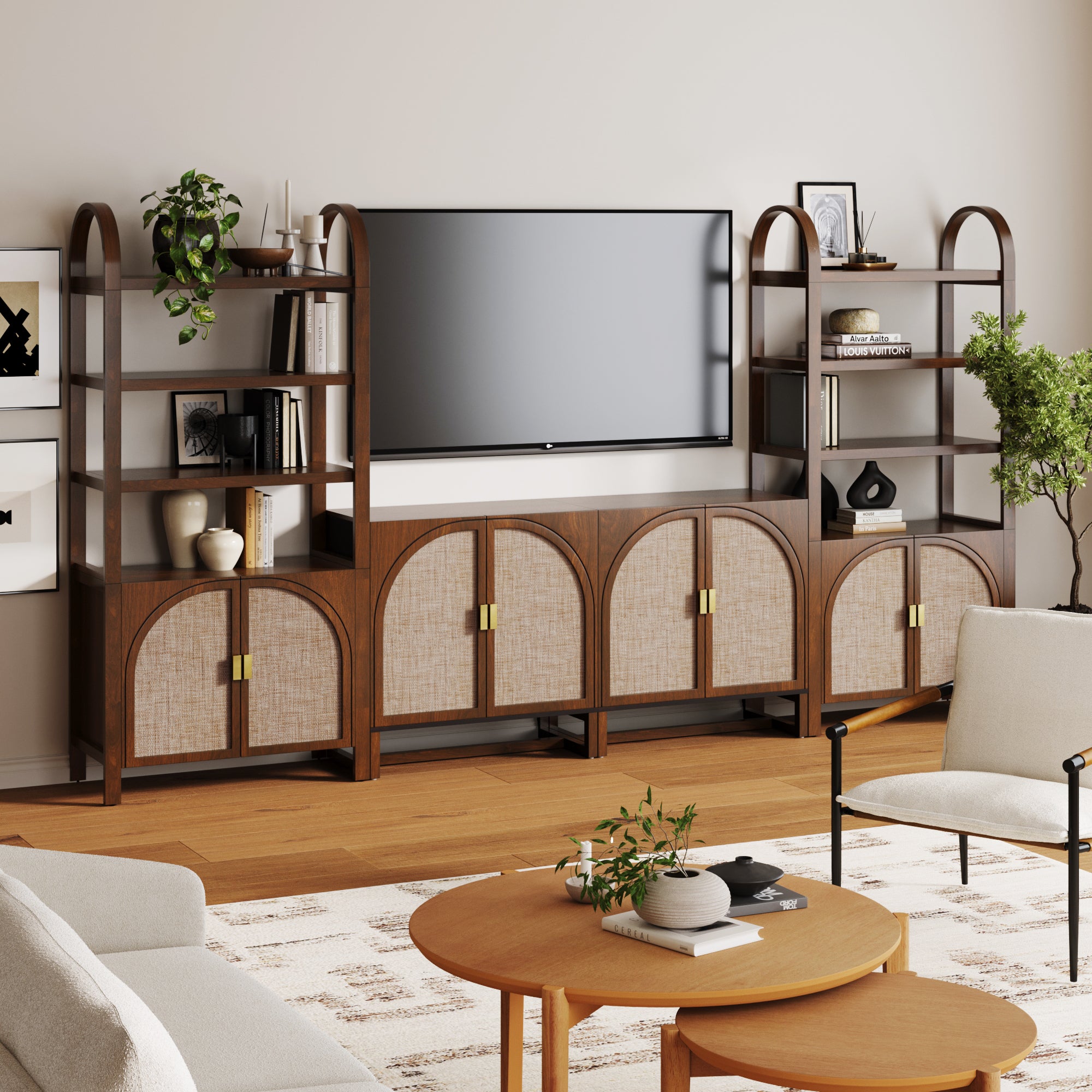 A modern living room with a wall-mounted TV, dark wood shelving units with arched tops, rattan cabinet doors, decorative objects, plants, a round coffee table, and neutral-toned chairs on a patterned rug.