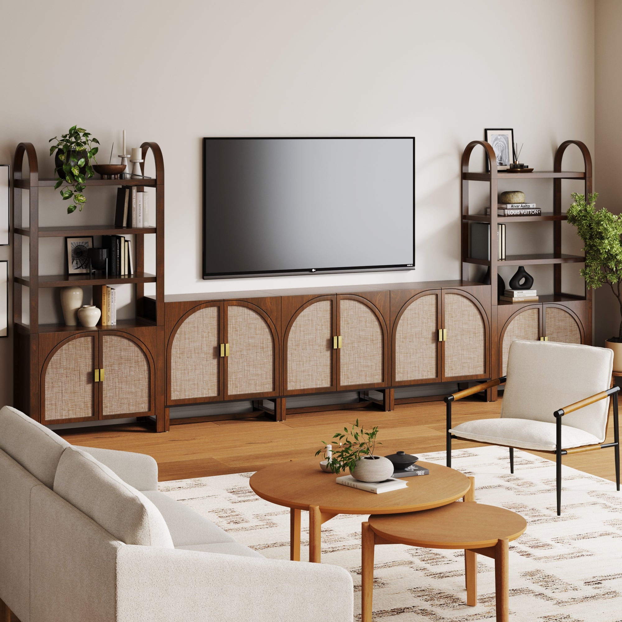 A modern living room features the Nathan James Arched Bookshelf Entertainment Center for 75 TV in Dark Acacia above a wood console with faux rattan doors, flanked by matching shelves, plus neutral seating and round coffee tables on a patterned rug.