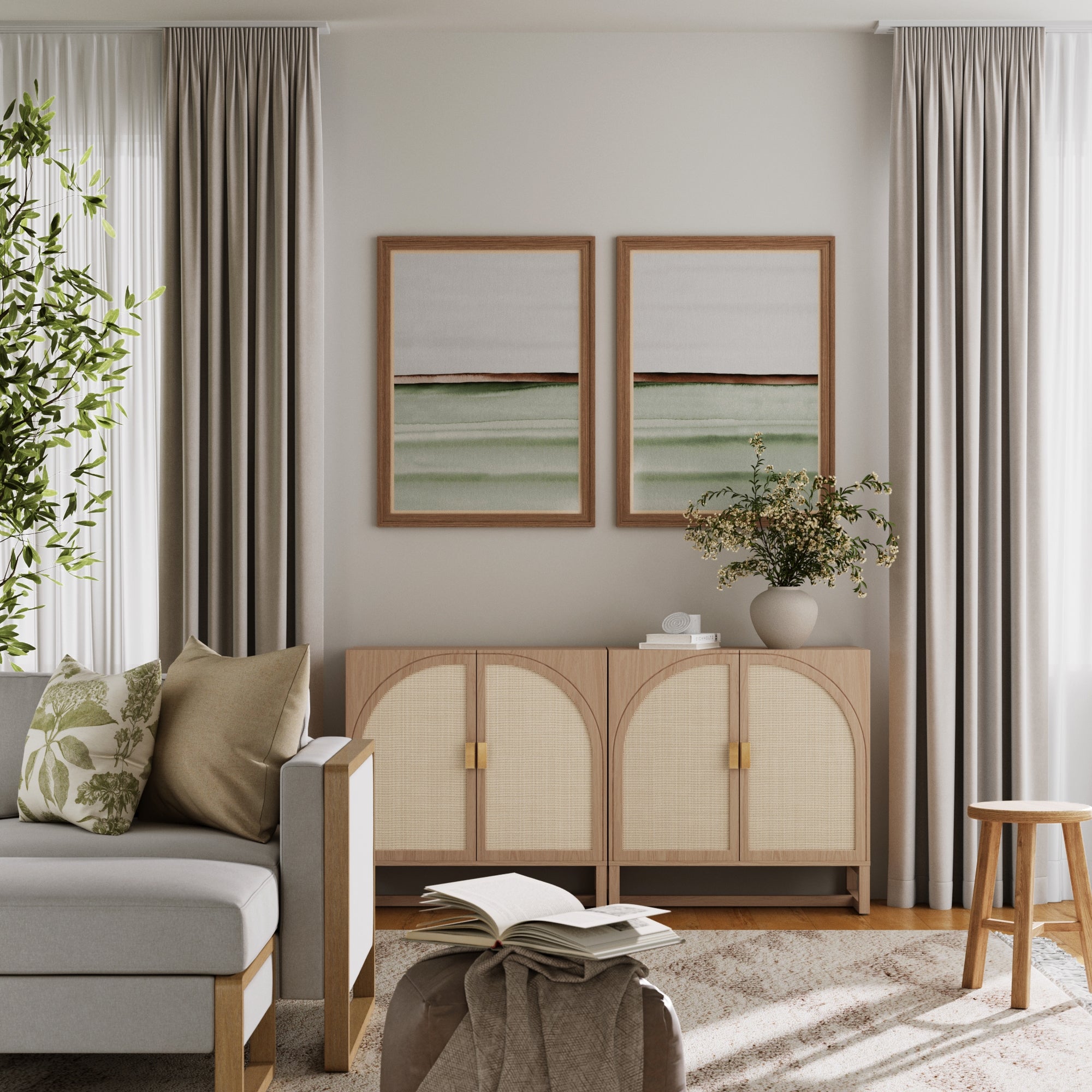A modern living room features a light gray sofa with green and beige cushions, neutral curtains, a potted plant, and two landscape paintings above the Nathan James Boho Arched TV Console Credenza Raw Oak (Set of 2); an open book rests on an ottoman.