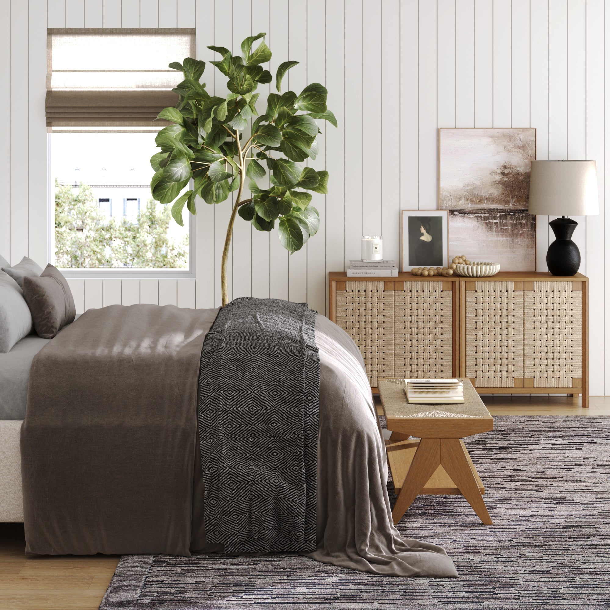 A modern bedroom features a large bed with neutral bedding, decor accents, framed art, a lamp, a tall potted plant, and natural light. The Nathan James Boho Woven Seagrass & Wood Storage Cabinet sits nearby, and a wooden stool is at the foot of the bed.