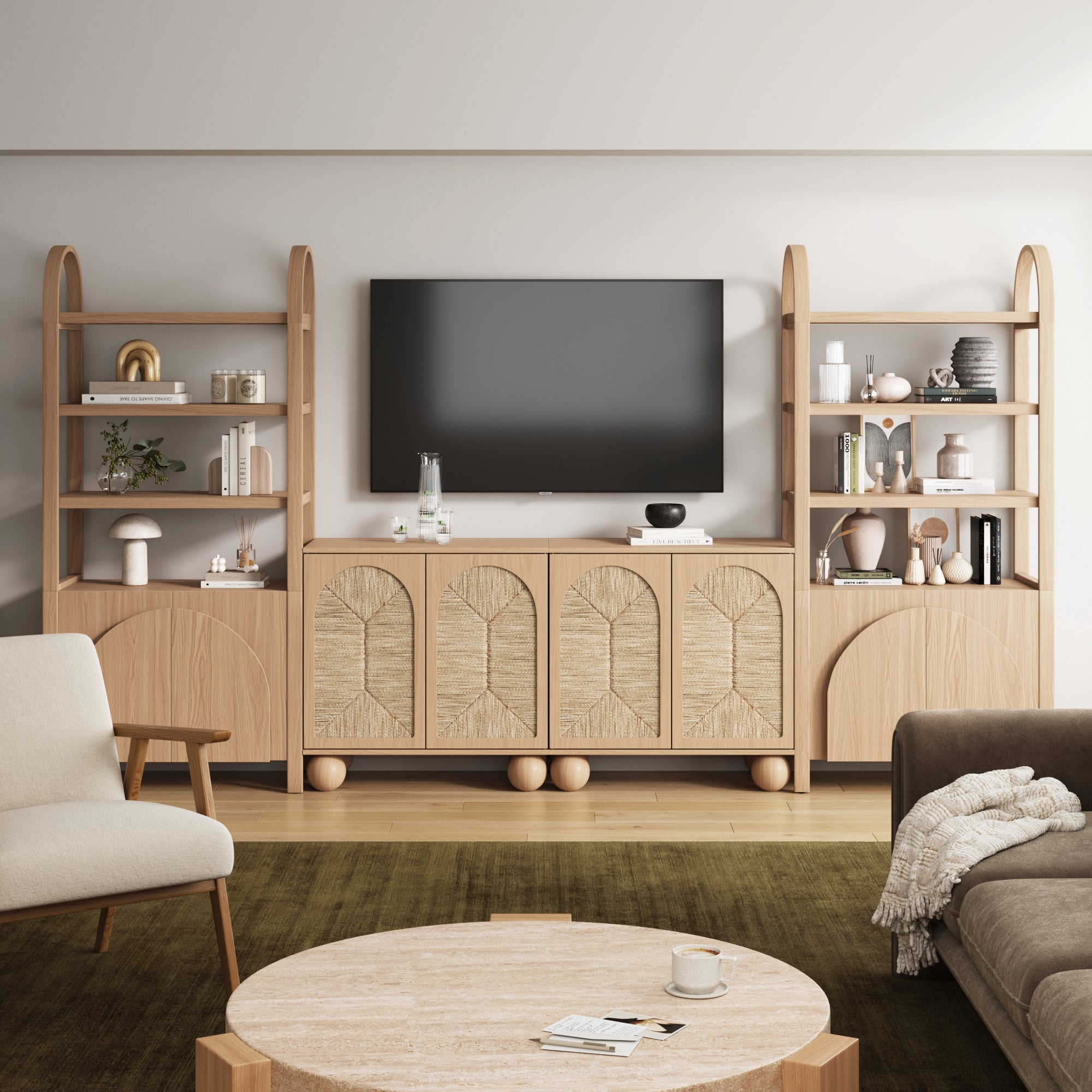 A modern living room featuring a wooden media console with arched cabinet doors, open shelves displaying decor items, a large wall-mounted TV, a beige armchair, a brown sofa, and a round coffee table on a green rug.