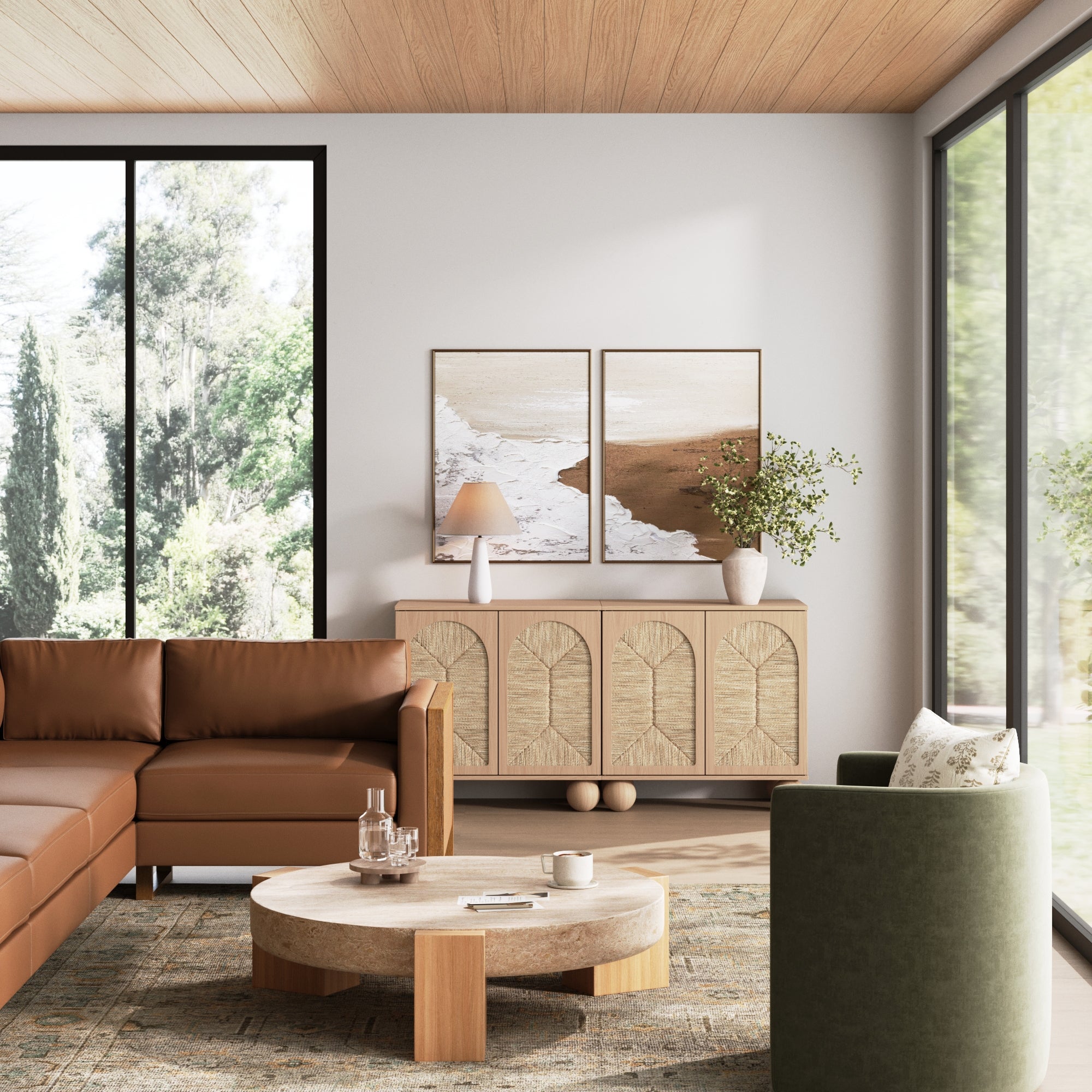 A modern living room features a brown sectional, round coffee table, green armchair, large windows with natural light, two framed artworks, and the Nathan James Seagrass Arched Storage Cabinet Raw Oak for calm, minimalist style and adjustable shelving.