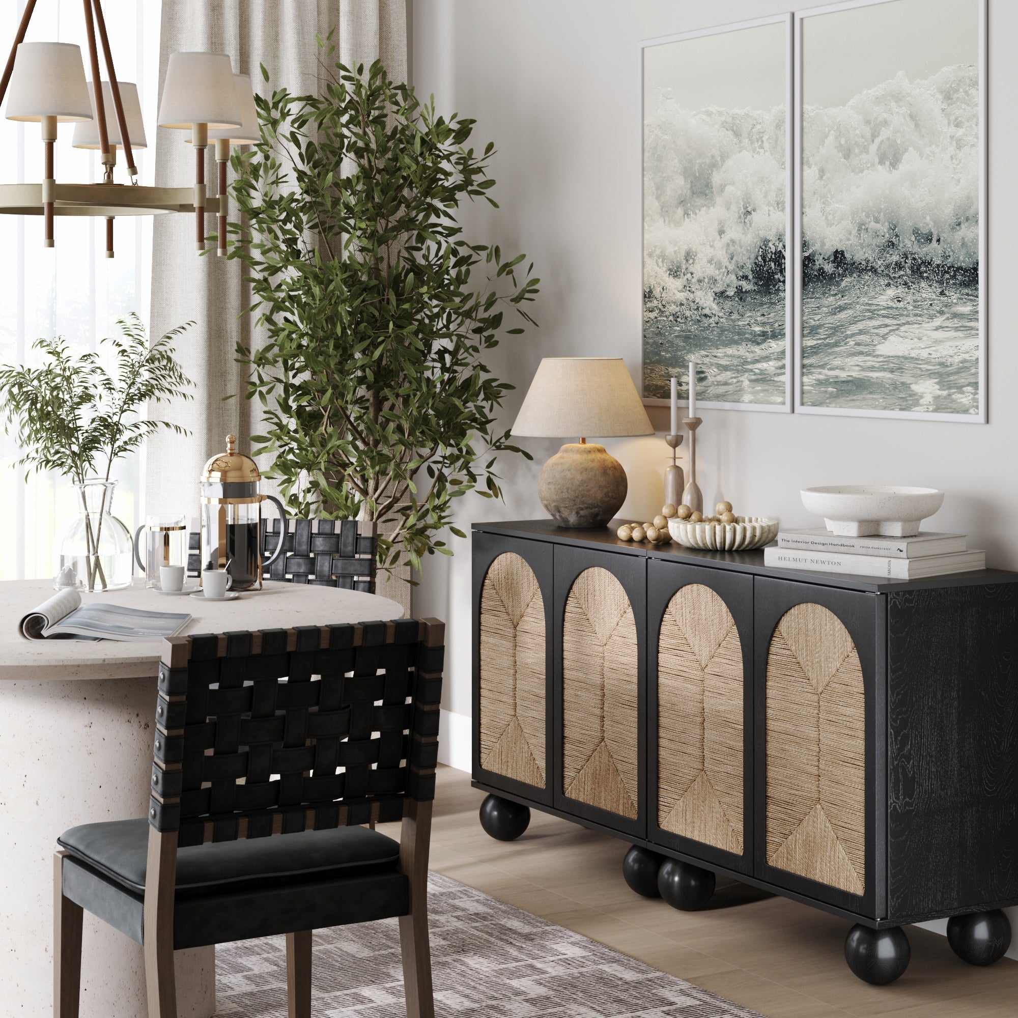A cozy dining area with a round table, woven-back chair, potted plant, and two Nathan James Seagrass Arched TV Console Credenzas in black. Boho decor includes a coffee set, table lamp, candles, and ocean waves wall art.