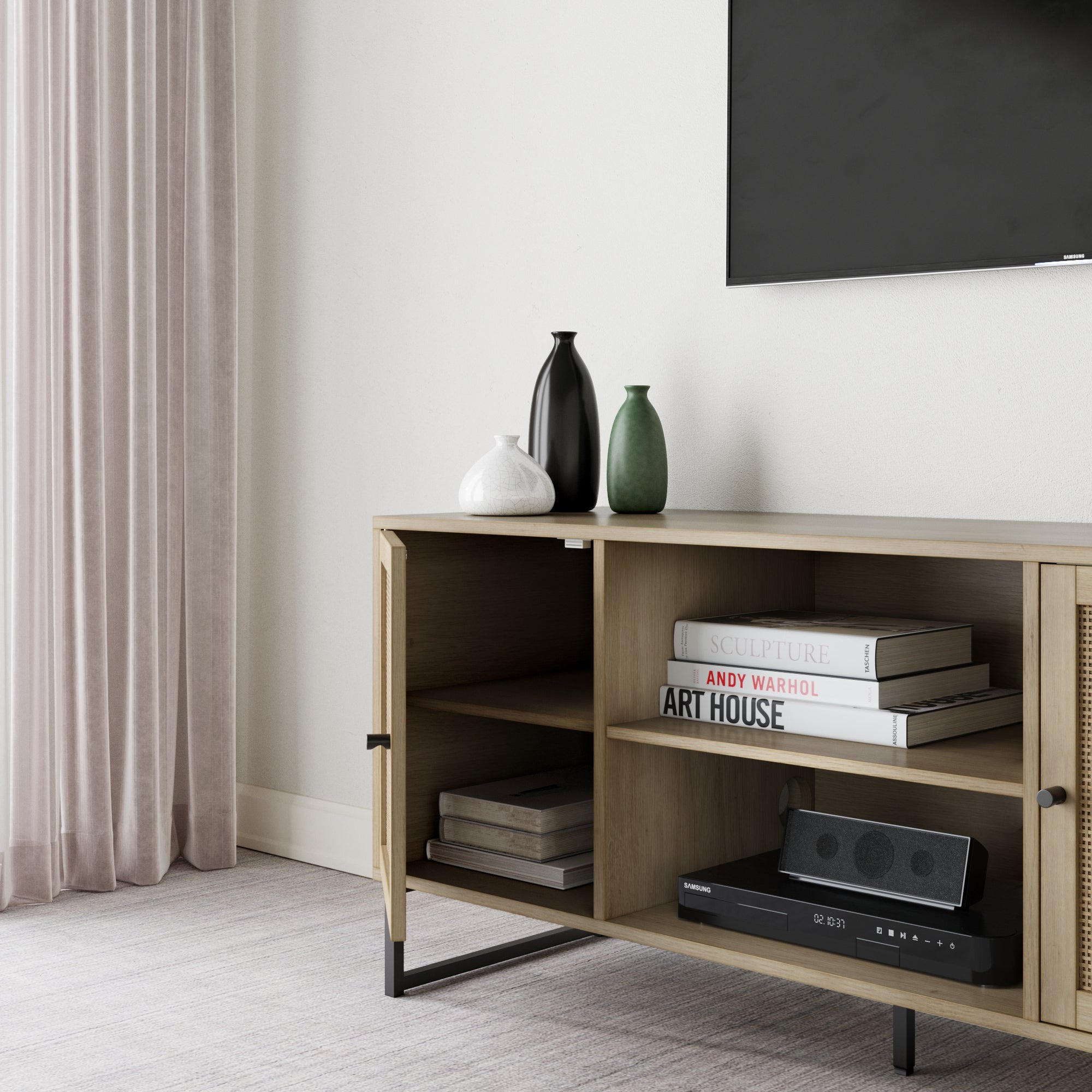 A modern living room with a light wood cabinet holding books, two vases, and a speaker, next to closed beige curtains and a wall-mounted TV. The decor is minimal and neutral-toned.