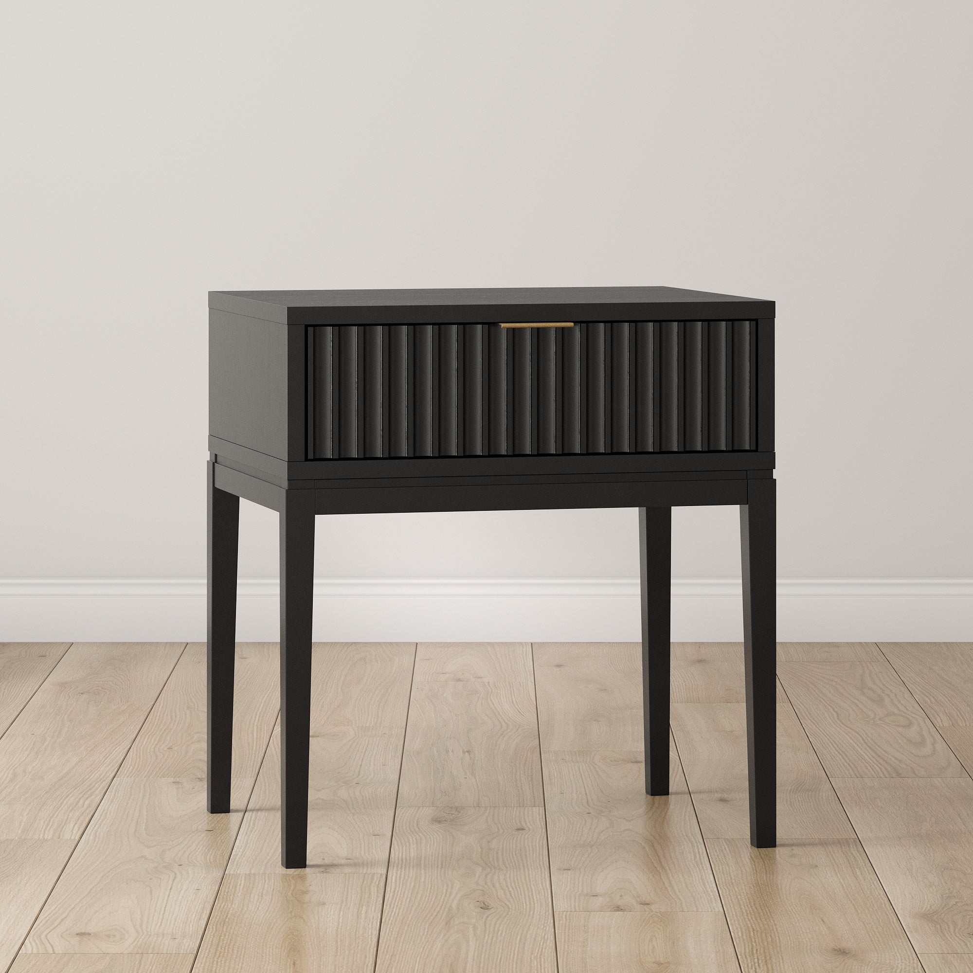 The Nathan James Mid-Century Fluted Nightstand in black oak, featuring slender legs, stands on a light wood floor against an off-white wall.