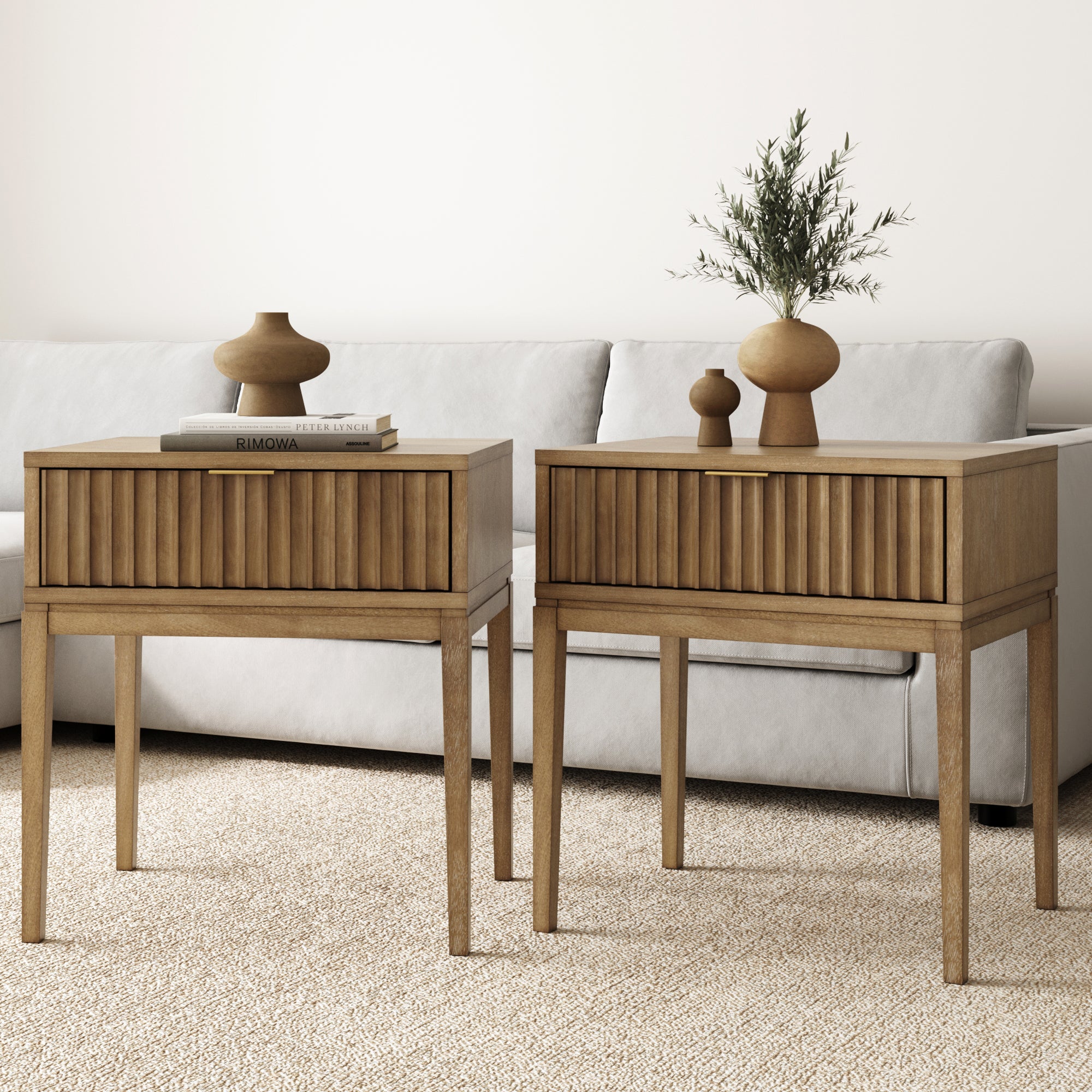 The Nathan James Bohemian Solid Wood Nightstand Set of 2 with Drawer in light brown stands on a beige carpet by a light gray sofa, each topped with vases, a book, and plants—beautifully elevating your bedroom furniture.