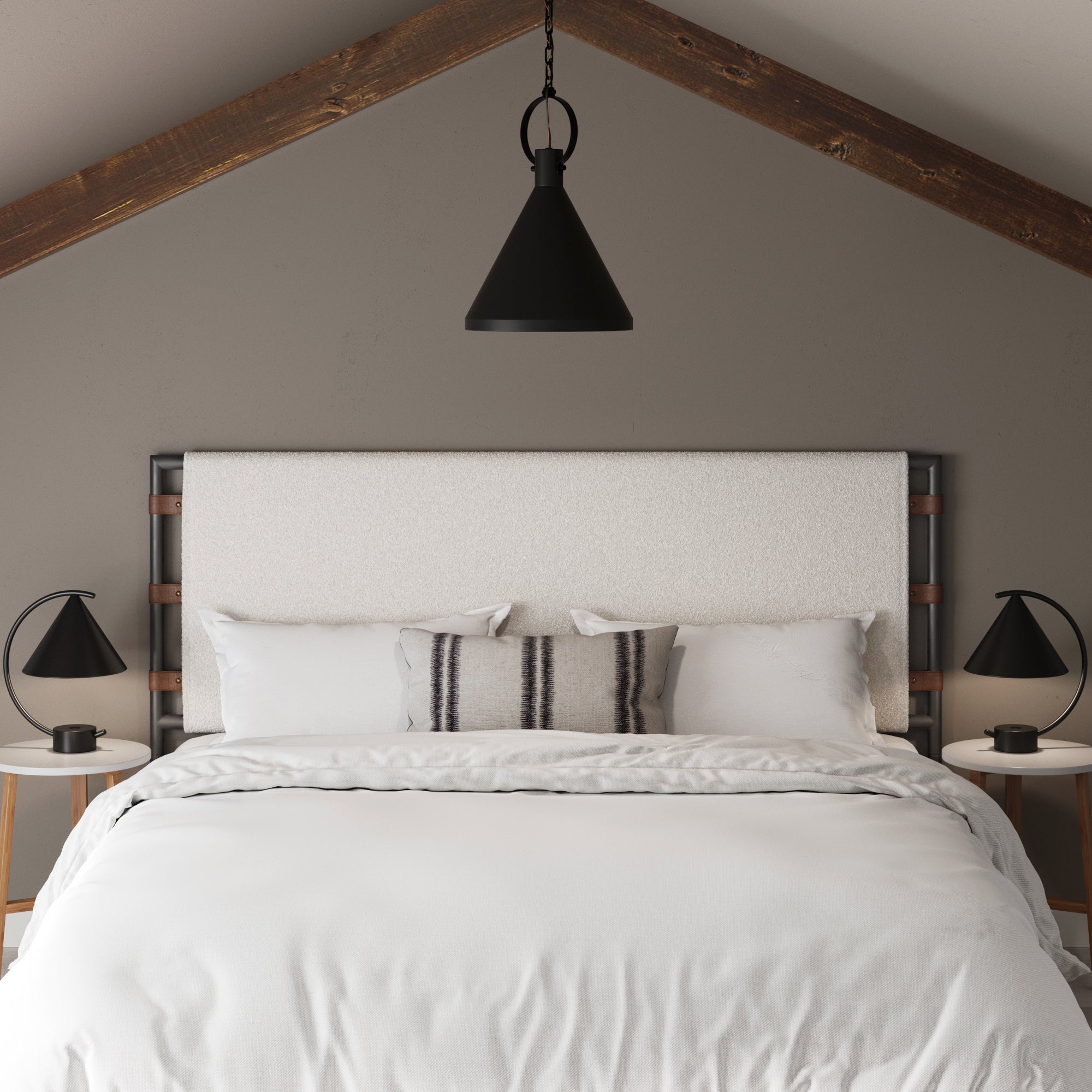 A bed with white bedding and a Nathan James Boucle King Upholstered Headboard features a striped accent pillow, black lamps on white nightstands, and a black pendant light under a sloped wooden ceiling.