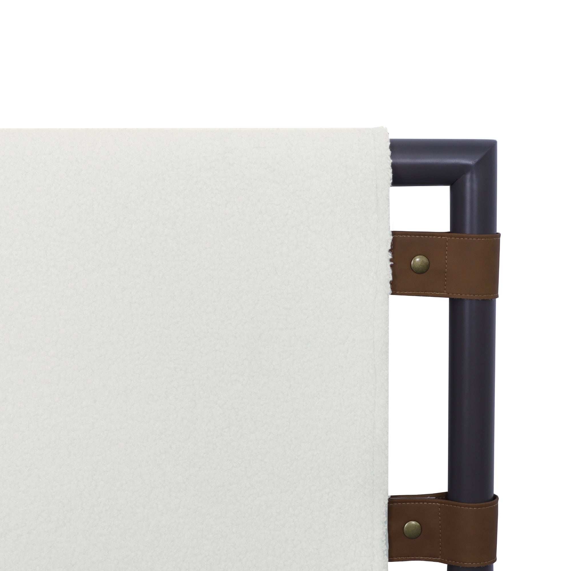 A close-up of a modern bed headboard with a soft white upholstered panel attached to a dark metal frame using brown leather straps with brass studs.