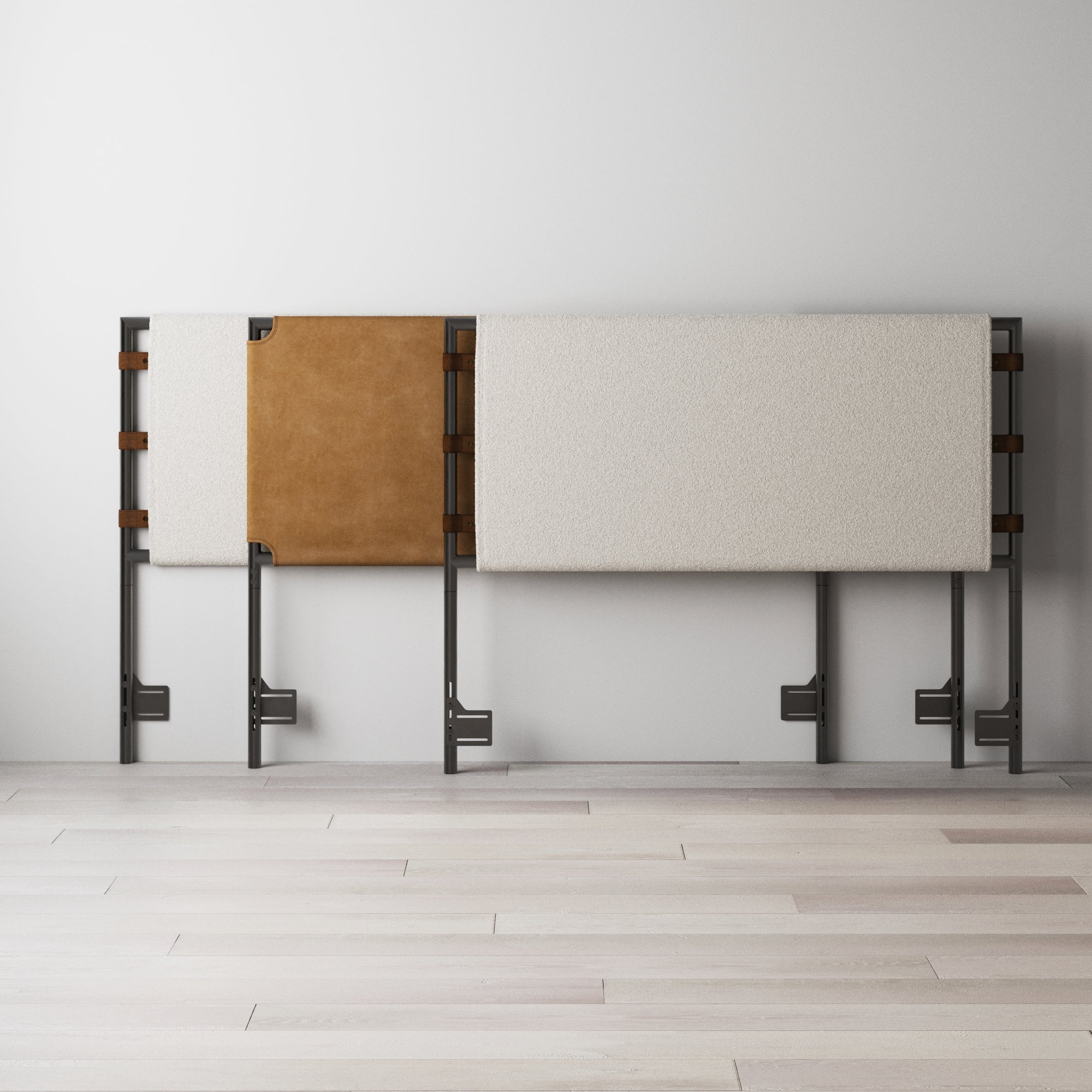 A modern headboard with a metal frame, featuring two rectangular padded panels—one in white fabric and a smaller one in brown leather—leaning against a plain white wall on a light wooden floor.