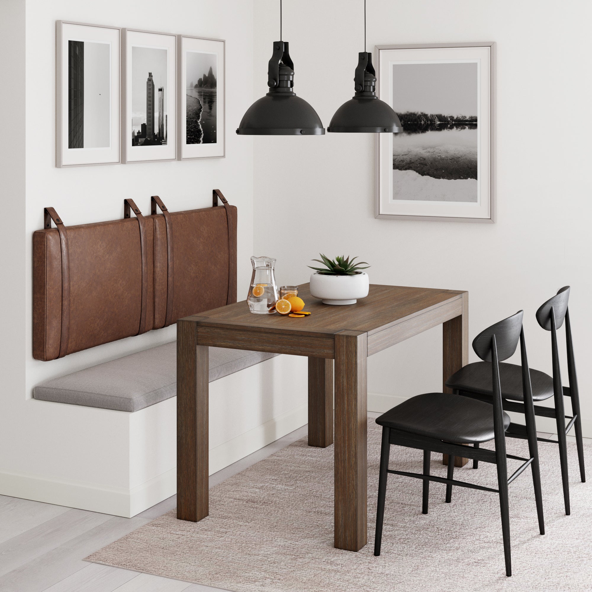 A modern dining area with a wooden table, three black chairs, a cushioned bench with brown backrests, hanging black pendant lights, framed wall art, a glass of water with orange slices, and a potted plant centerpiece.