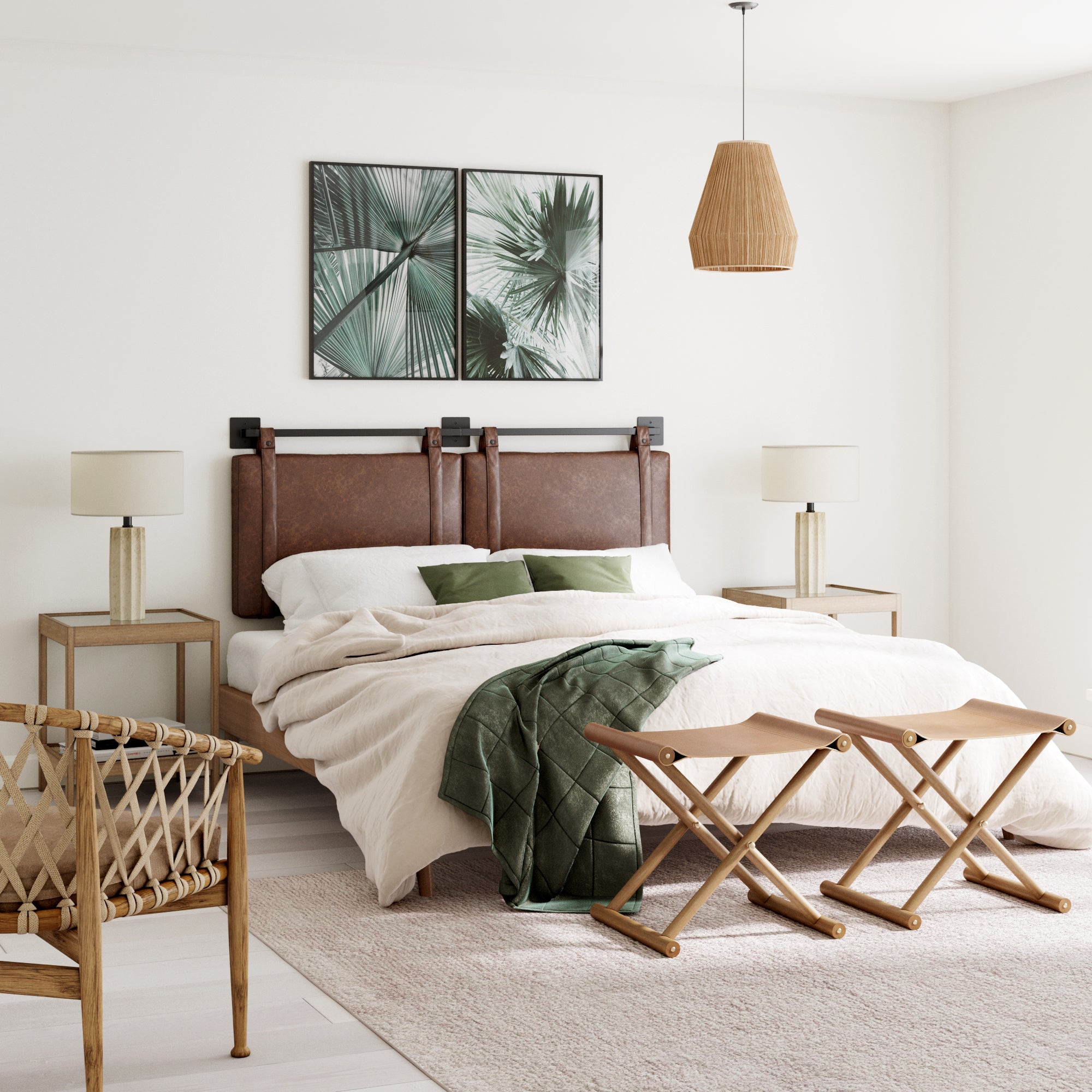 A bright, minimal bedroom featuring the Nathan James Upholstered Queen Wall Mount Headboard in brown vegan leather, neutral bedding, a green throw, wood furniture, two matching lamps, a wicker chair, and palm leaf artworks above the bed.