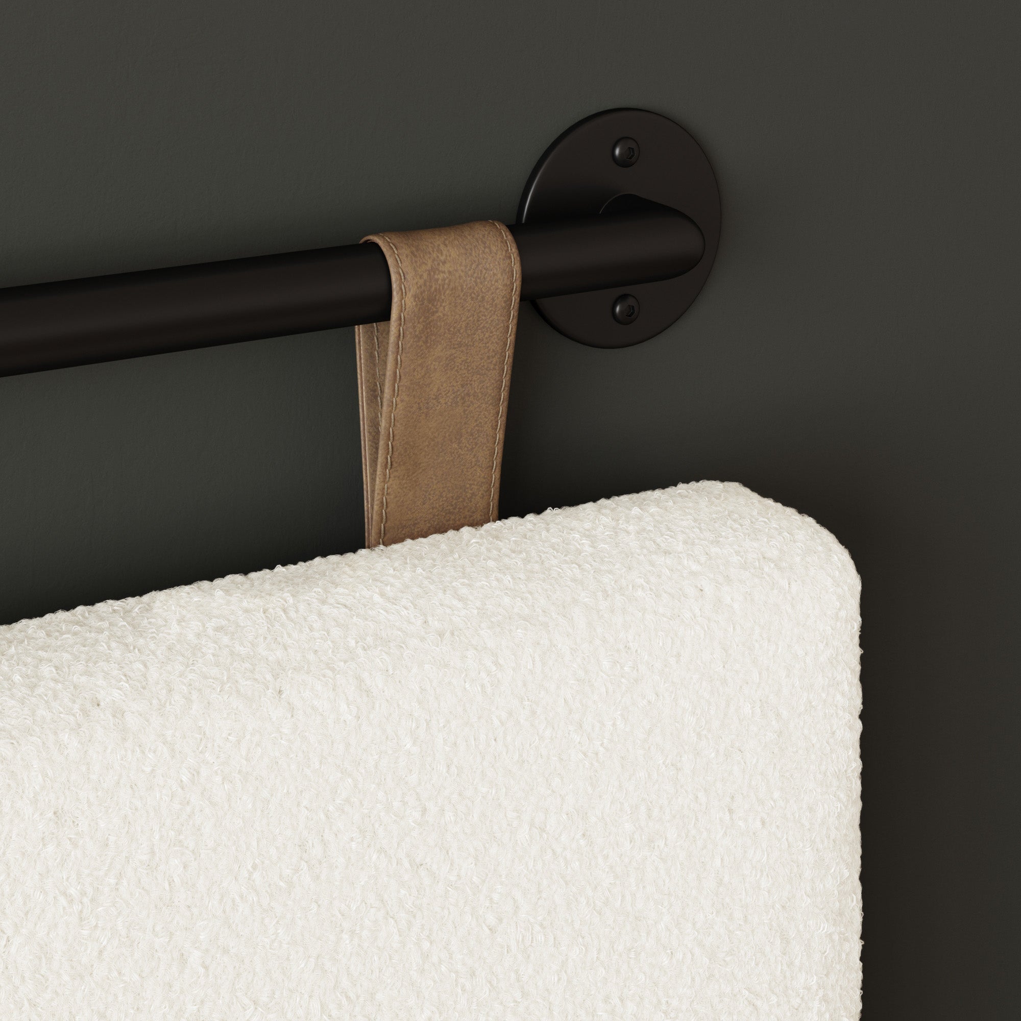 A close-up of a fluffy white towel with a tan leather loop hanging on a black metal towel bar mounted on a dark wall.