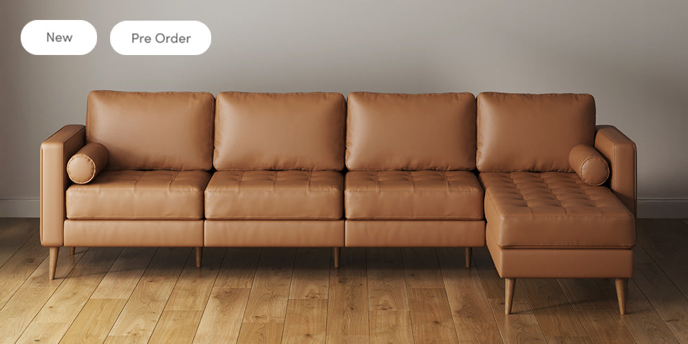 A modern brown leather sectional sofa with wooden legs is placed on a light wooden floor against a plain beige wall. Two buttons labeled New and Pre Order appear in the upper left corner.