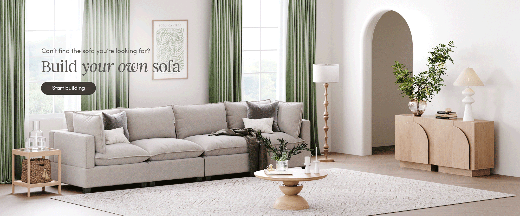 A bright living room with a large gray sectional sofa, round coffee table, side table, and light wood cabinet; green curtains and plants add a fresh touch. Text reads: Build your own sofa. Start building.