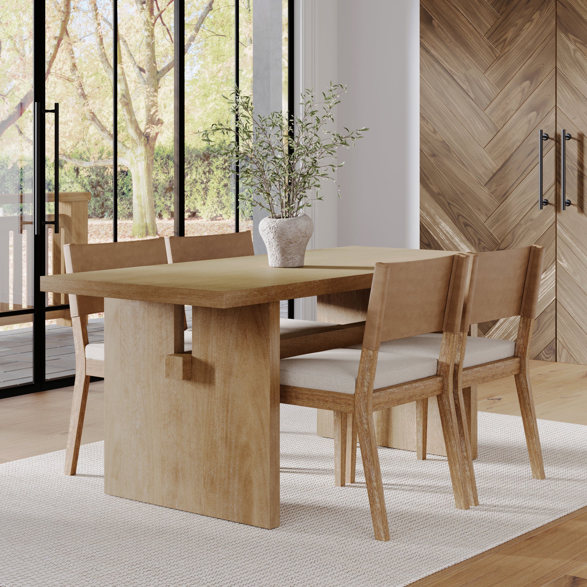 A modern dining room featuring the Nathan James Farmhouse Dining Set— a light solid wood table with four matching chairs, a white vase with green branches, large windows framing trees outside, and a wood-patterned wall.