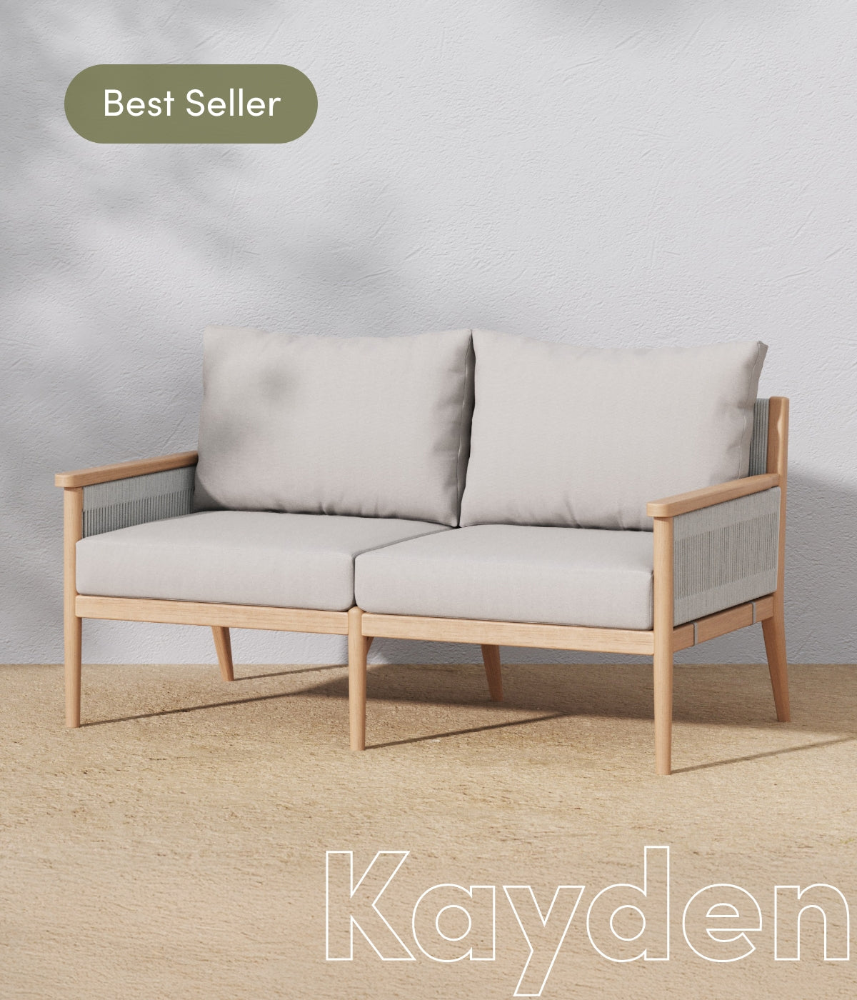 A modern wooden loveseat with light gray cushions sits against a textured white wall on a beige floor. A green Best Seller label is in the top left corner, and “Kayden” is written in large outlined letters at the bottom right.