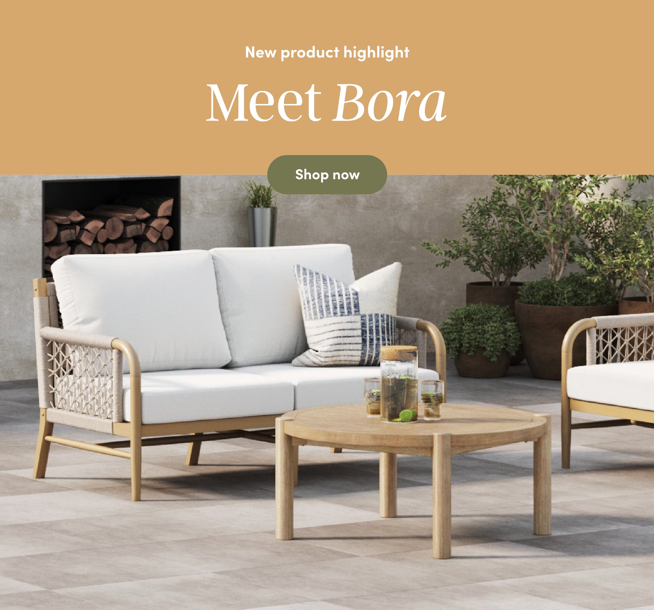 Outdoor patio set with a woven loveseat featuring white cushions, a round wooden coffee table with drinks and a pitcher, a cushion, and decorative plants in the background. Text reads: Meet Bora. Shop now.