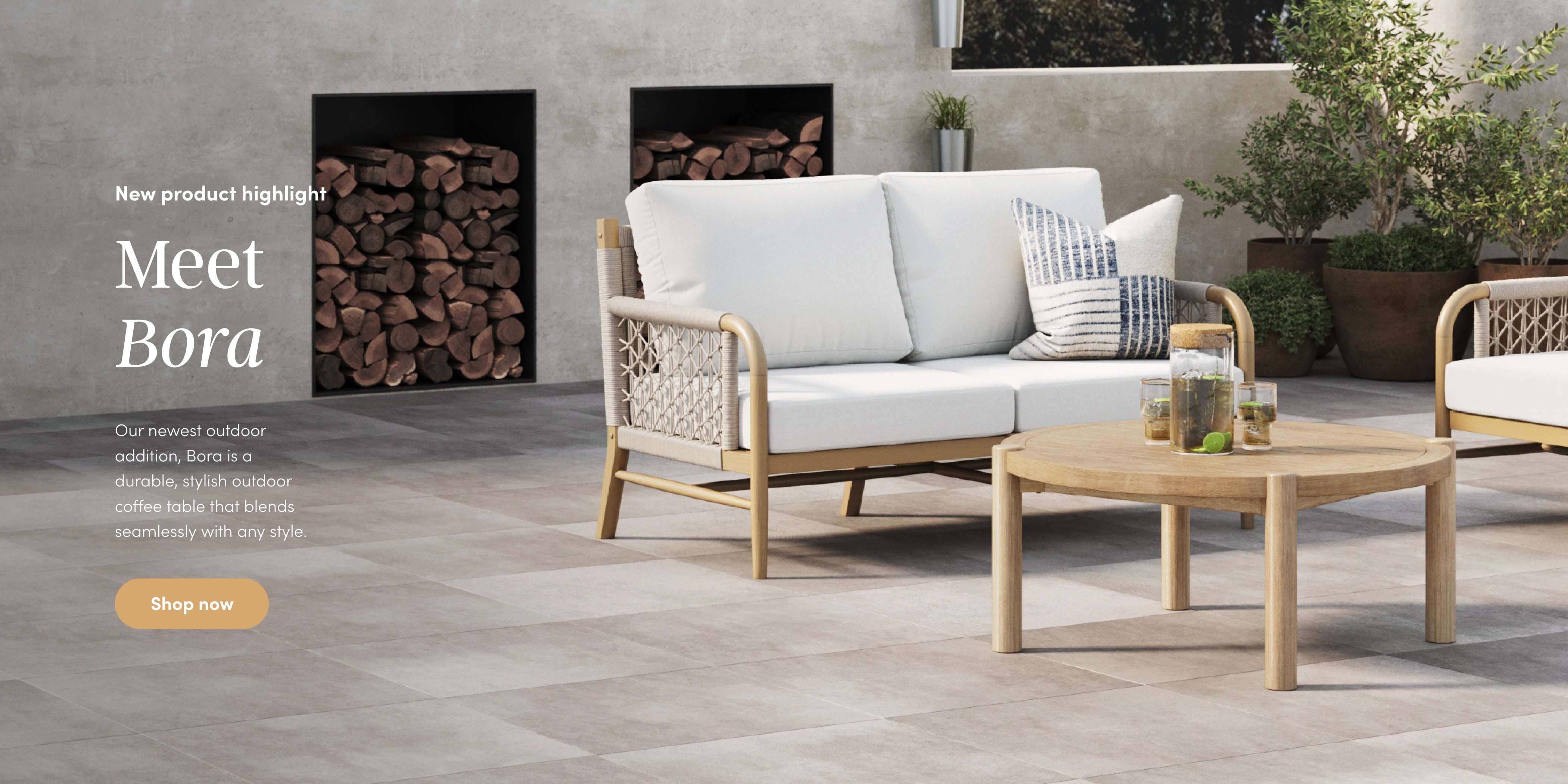 A modern outdoor patio with light tile flooring, featuring a cushioned sofa, a round wooden coffee table, plants, and firewood stacked in black shelves against a neutral wall. Text highlights the Bora furniture collection.