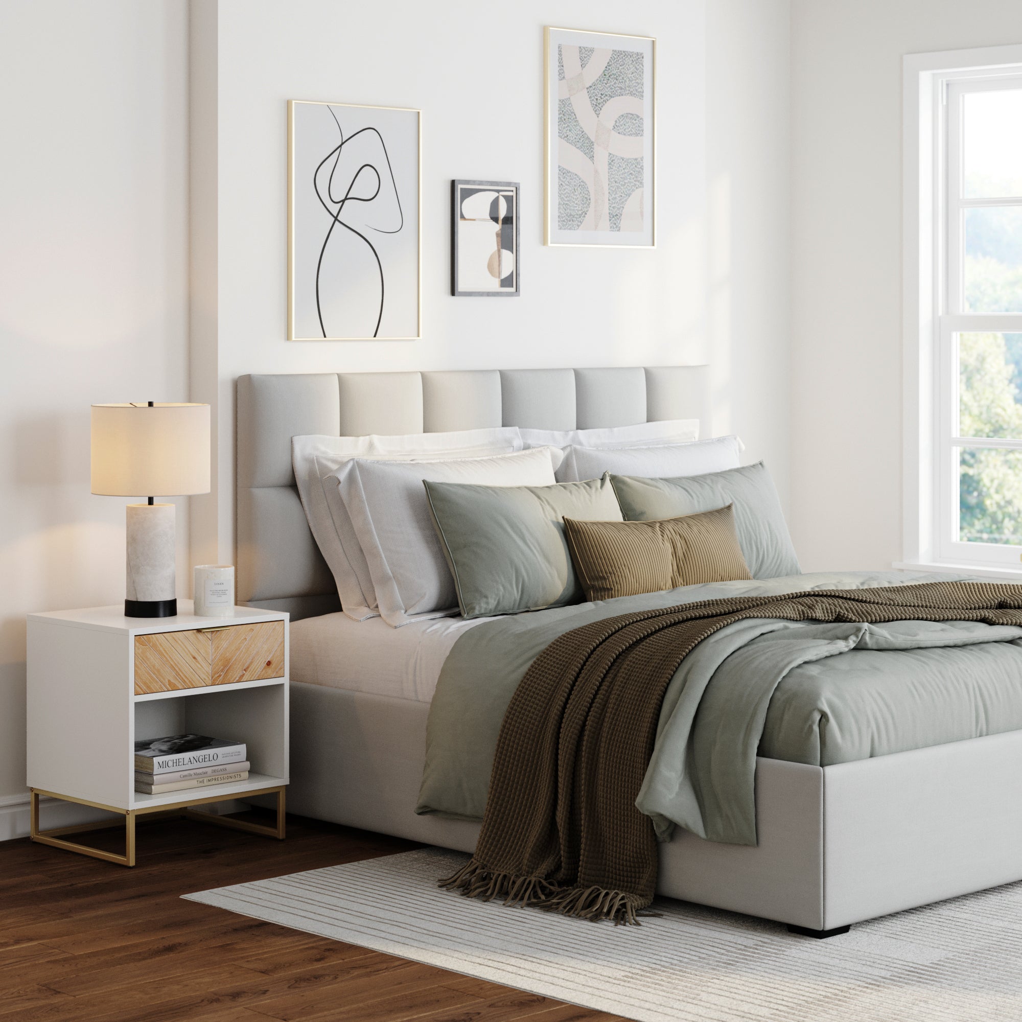 Modern bedroom with a gray upholstered bed, green and beige bedding, a brown throw blanket, a white nightstand with a lamp, and abstract art on white walls. Sunlight streams in through a large window.