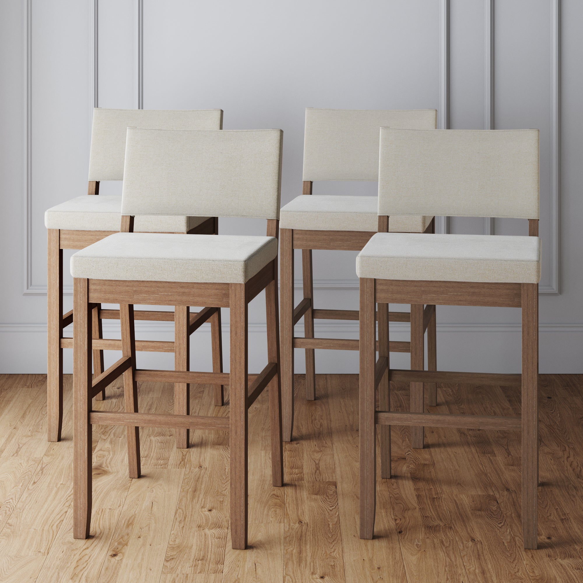 Set of 4 Nathan James Wood Upholstered Bar Stools in light brown with cushioned seats and backs, featuring wooden legs, displayed on a light wood floor against a light gray paneled wall.