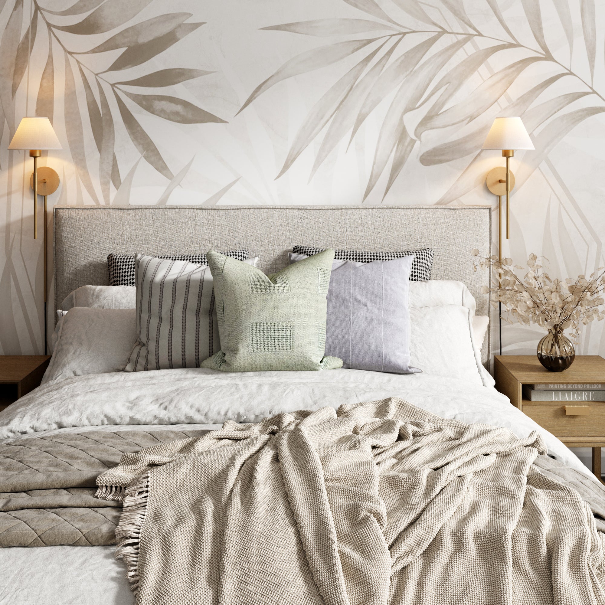 A modern bedroom with a neatly made bed featuring neutral-toned pillows and blankets. There are two wooden nightstands with lamps and dried floral arrangements, and a leafy-patterned wallpaper accent wall behind the headboard.