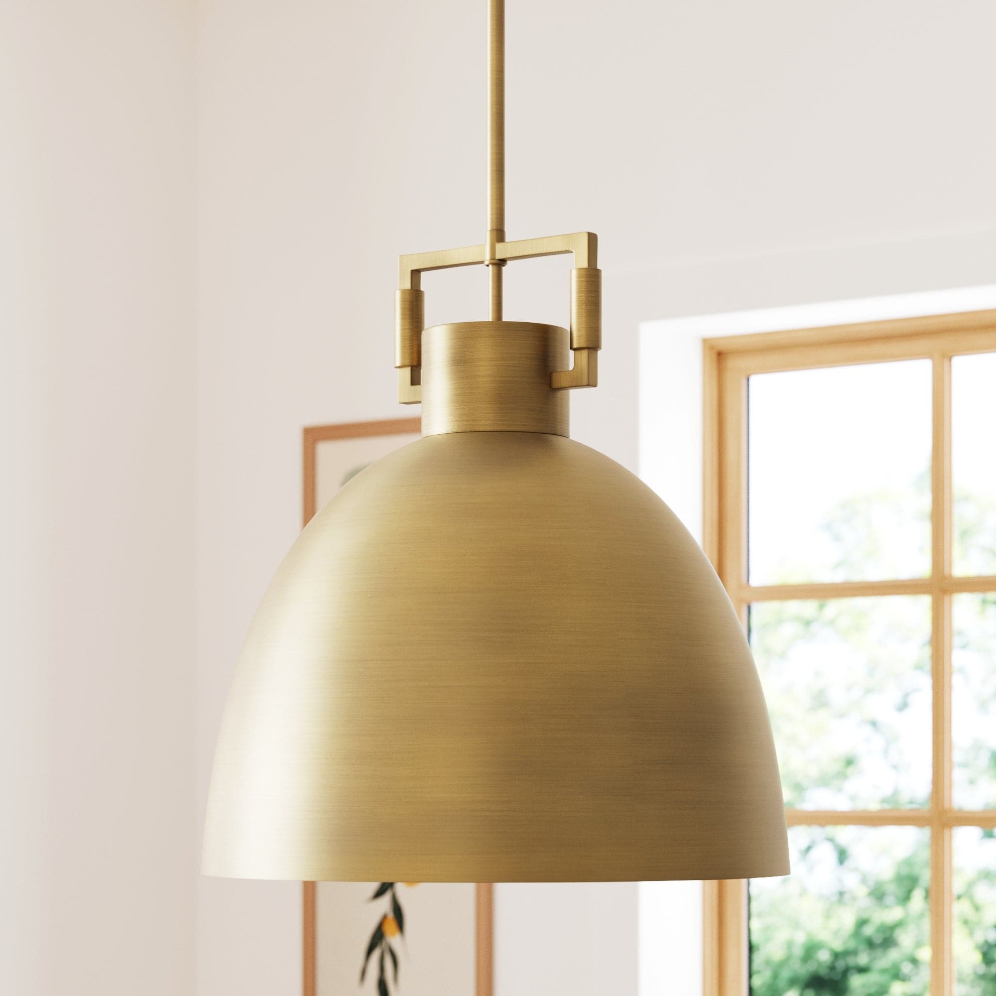 The Nathan James Metal Dome Shade Pendant Ceiling Light in brass hangs from the ceiling of a bright room featuring a large window and framed wall art in the background.