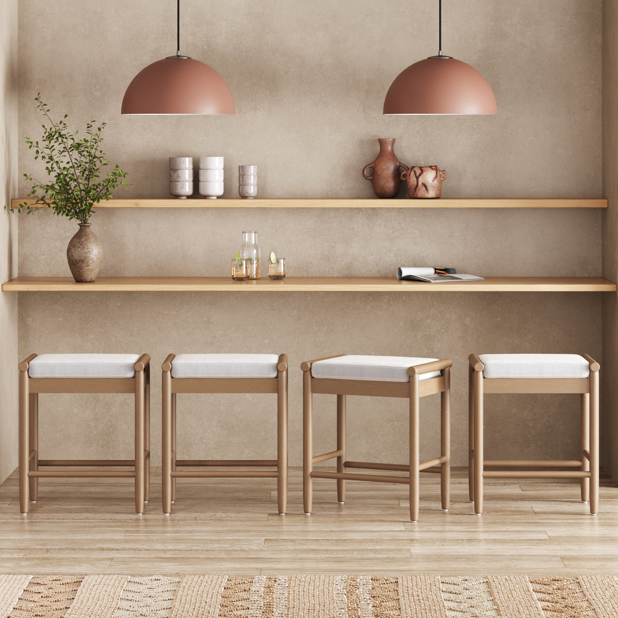 A minimalist kitchen showcases four Nathan James Backless Wooden Bar Stools with Boucle Upholstery in light brown, two wooden shelves with ceramics, glassware, a vase plant, and two dome pendant lights against a beige textured wall.