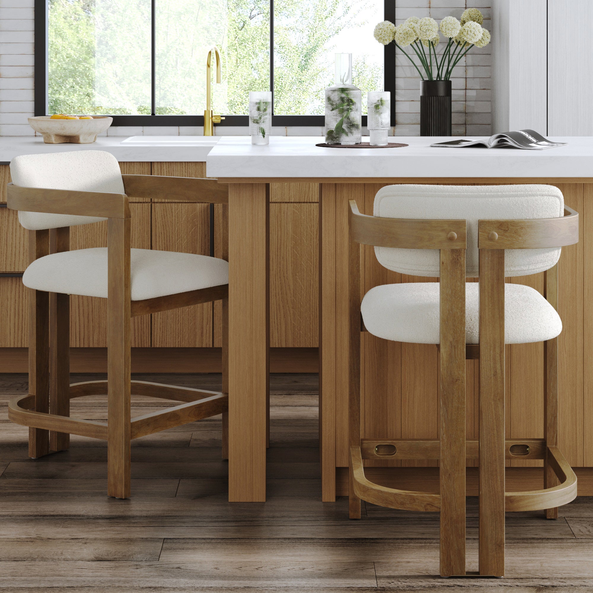 Two Nathan James Barrel Bar Stools with backs and arms in light brown, featuring white upholstered seats, are set at a kitchen island with a white countertop. A window overlooks greenery, and décor accents the counter. Set of 2.