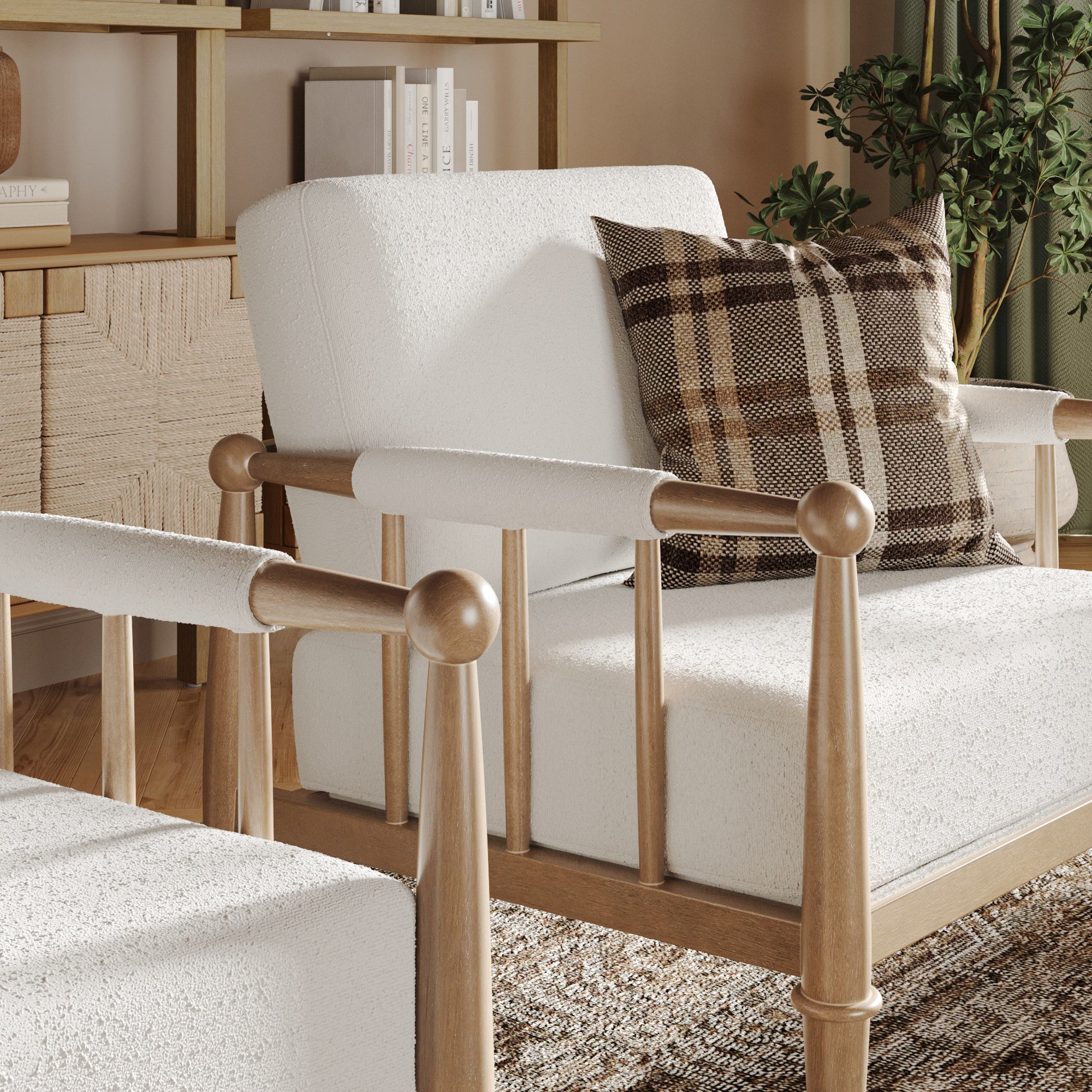 A cozy, modern armchair with light wood frame and white upholstery sits in a sunlit living room. A brown plaid pillow rests on the seat, with bookshelves, a sideboard, and a potted plant in the background.