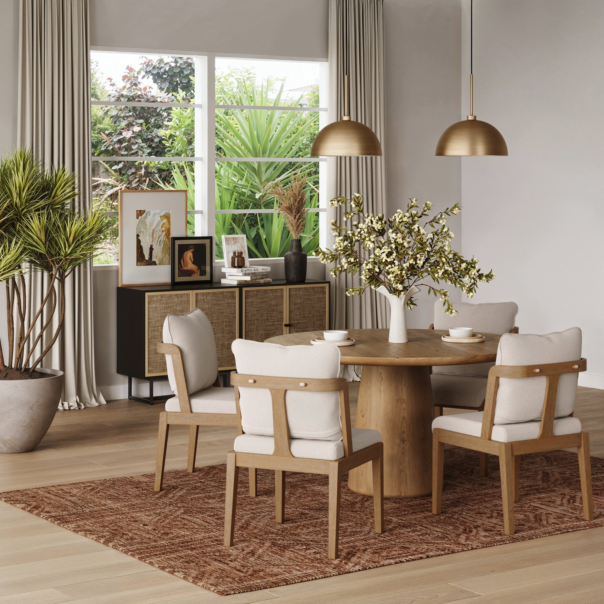 A modern dining room featuring a round wooden table, a Nathan James Scandinavian Dining Chair with Back Light Brown (Set of 4), a brown rug, plants, sideboard with framed art, and large windows offering views of greenery.