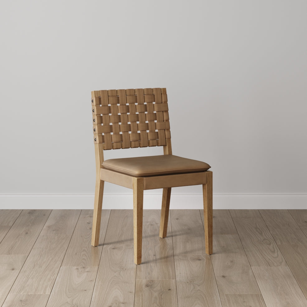 A wooden chair with a woven backrest and a cushioned seat sits on a light-colored wooden floor against a plain light gray wall.