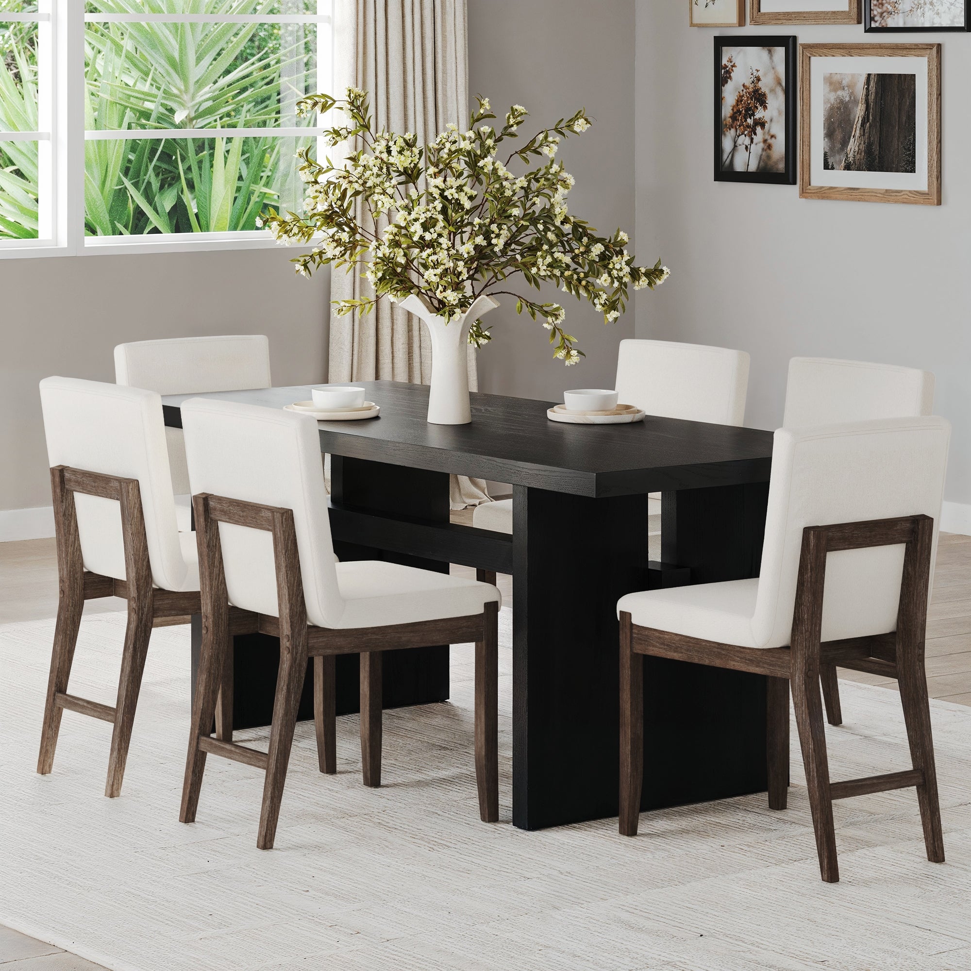 A Scandinavian dining room features a dark solid wood table surrounded by six Nathan James Exposed Back Dining Chairs in dark brown. A vase with white flowers centers the table, while large windows, wall art, and a light carpet complete the airy space.