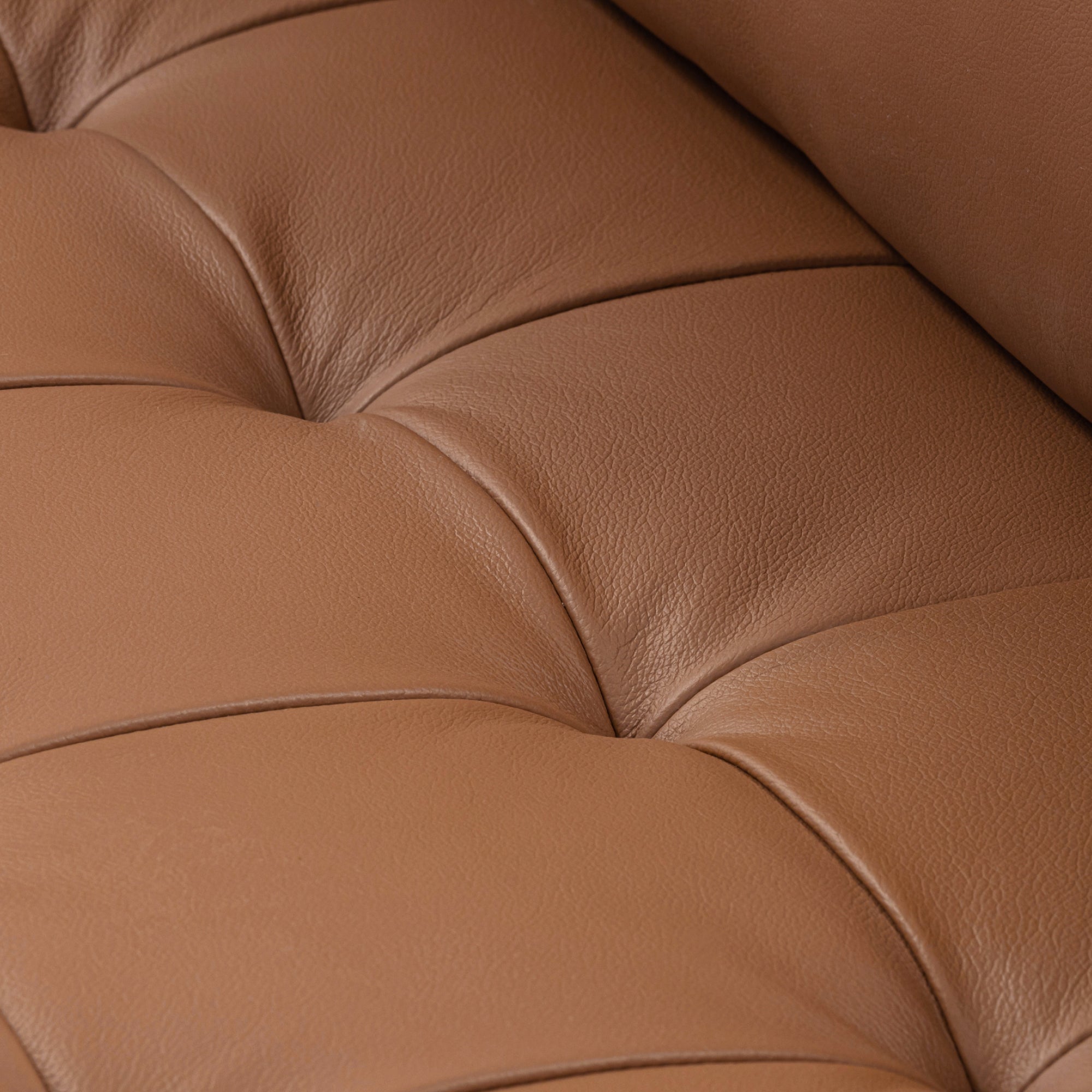 Close-up of tan brown leather upholstery with visible stitching and tufted details, showing the texture and smooth surface of the cushioned material.