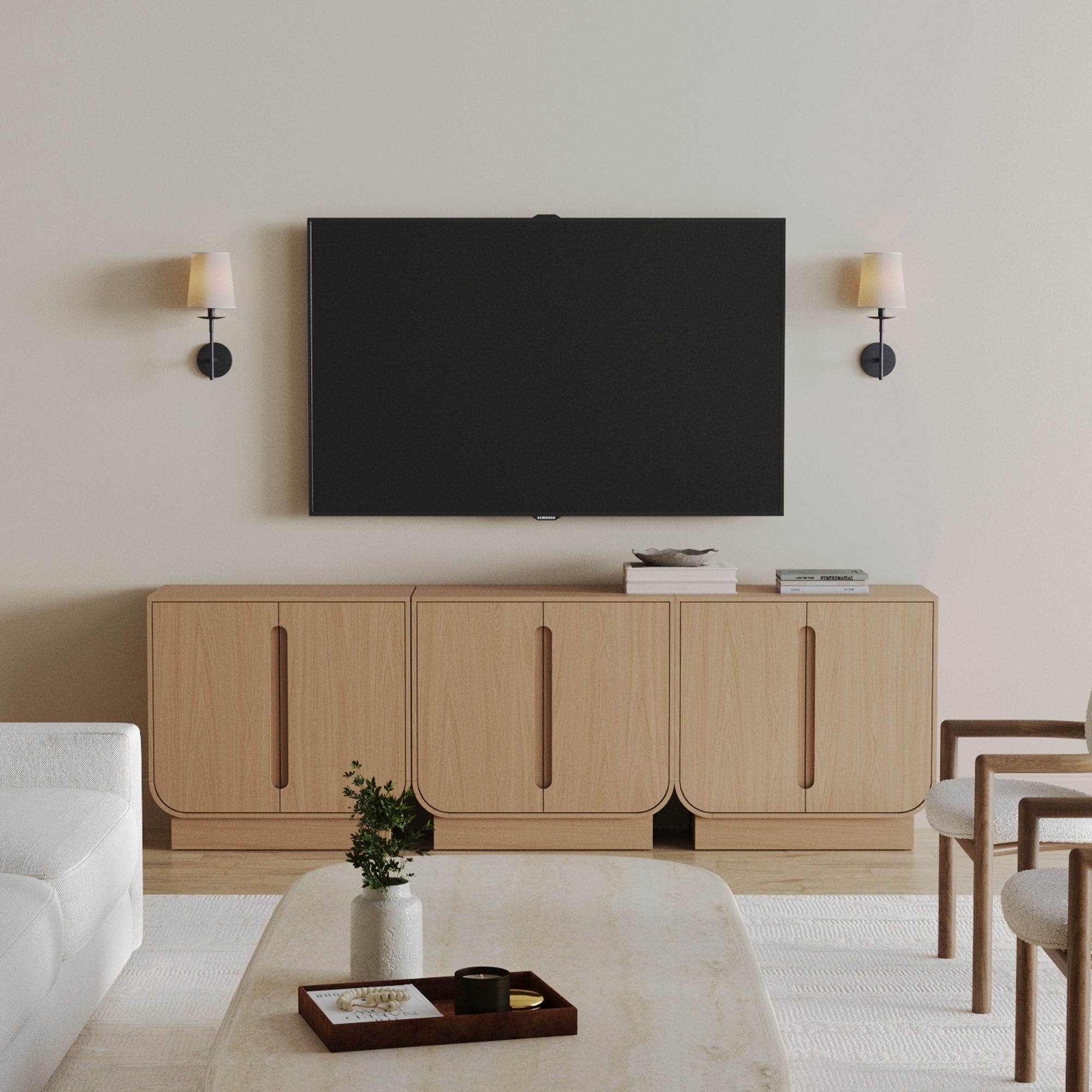 Minimalist living room with a wall-mounted TV above the Nathan James Veneer Arched Accent Cabinet or TV Stand Raw Oak (Set of 3), two modern sconces, a white sofa, marble coffee table with decor, and two wooden chairs.