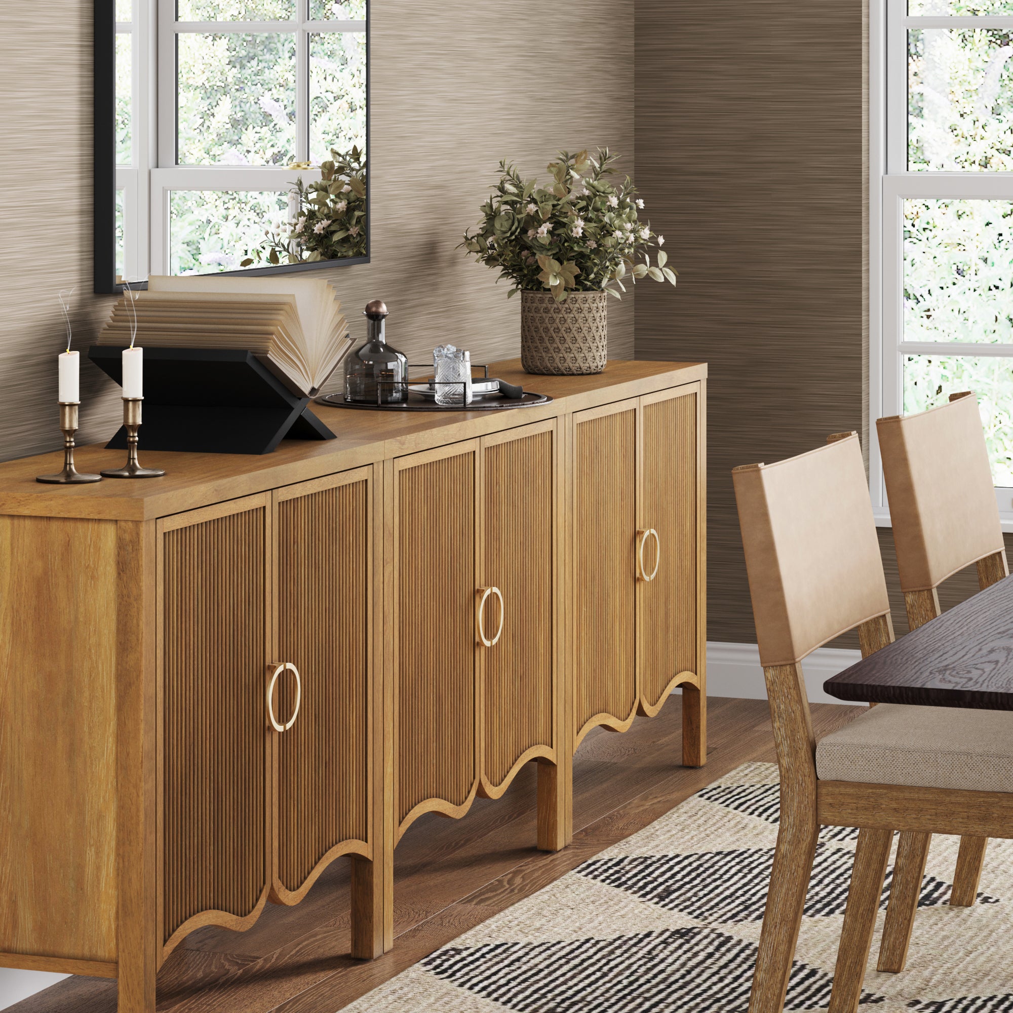 The Nathan James Transitional Fluted Cabinet or TV Stand (Set of 3, Light Brown) with gold handles stands by the wall, styled with candles, books, and a potted plant. Fluted doors add texture. A large mirror and part of a dining table are nearby.