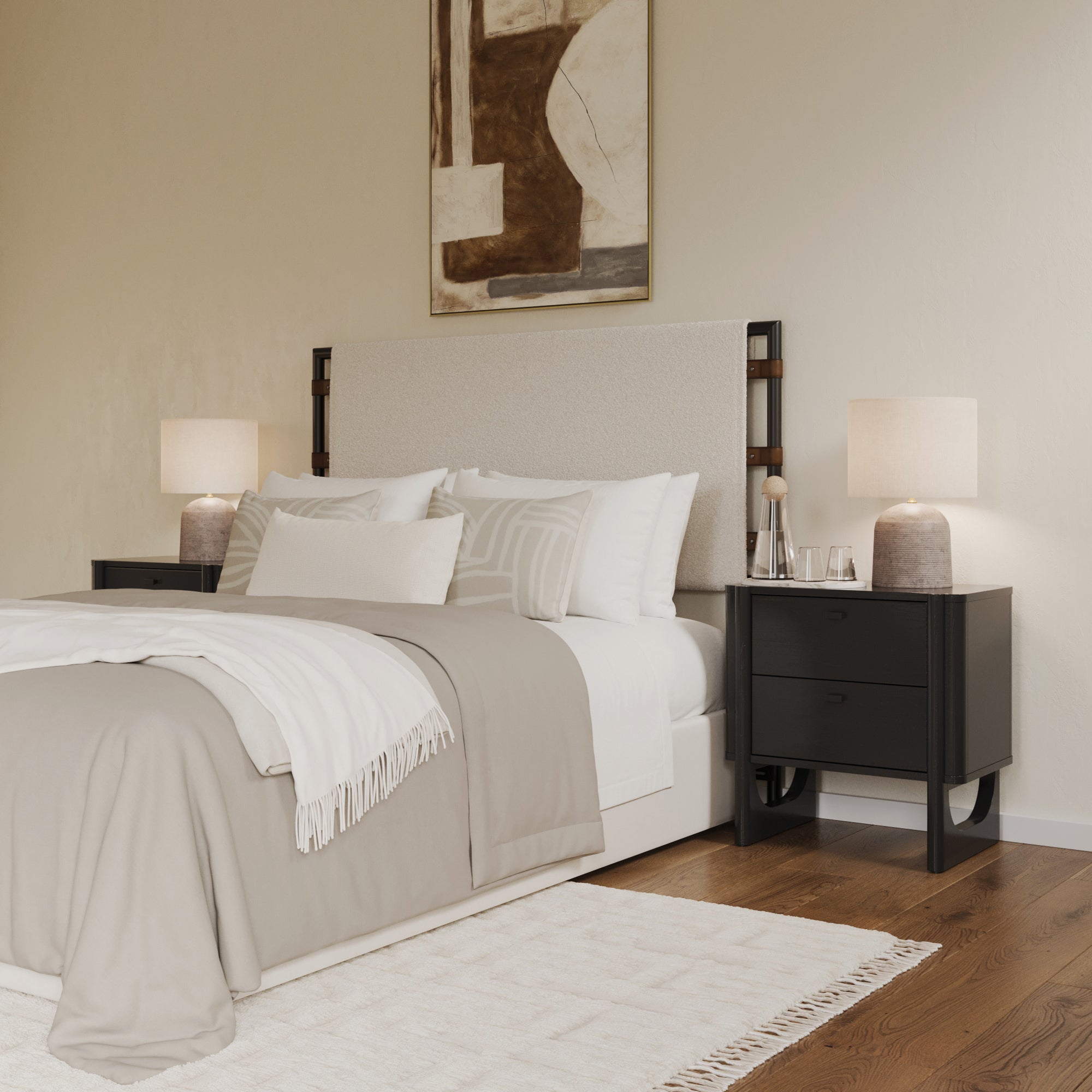 A modern bedroom with a beige upholstered bed, neutral bedding, two black nightstands with lamps, a white rug on wooden floors, and an abstract artwork on a cream-colored wall.