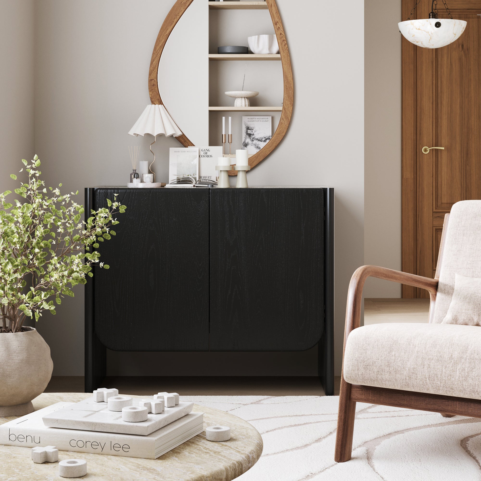A modern living room with light walls, a Nathan James Mid Century Modern Wood Curio Cabinet in black oak, round mirror, decorative items, beige armchair, marble coffee table with books and chess pieces, potted plant, and wooden door.