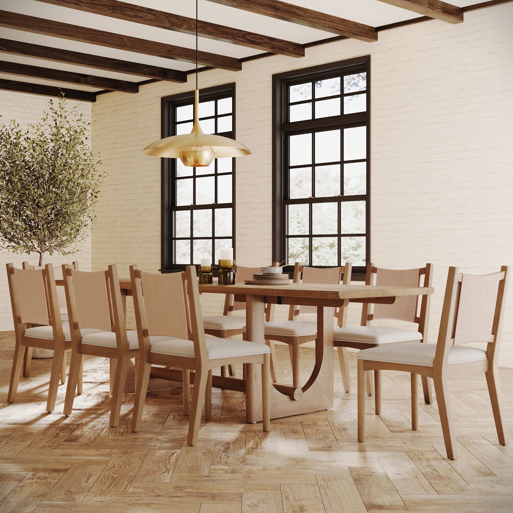 A modern dining room featuring the Nathan James Wood Dining Room Table with Leaf Extension for 8, eight beige cushioned chairs, a gold pendant light, large windows, light wood floors, white brick walls, and a potted tree in the corner.