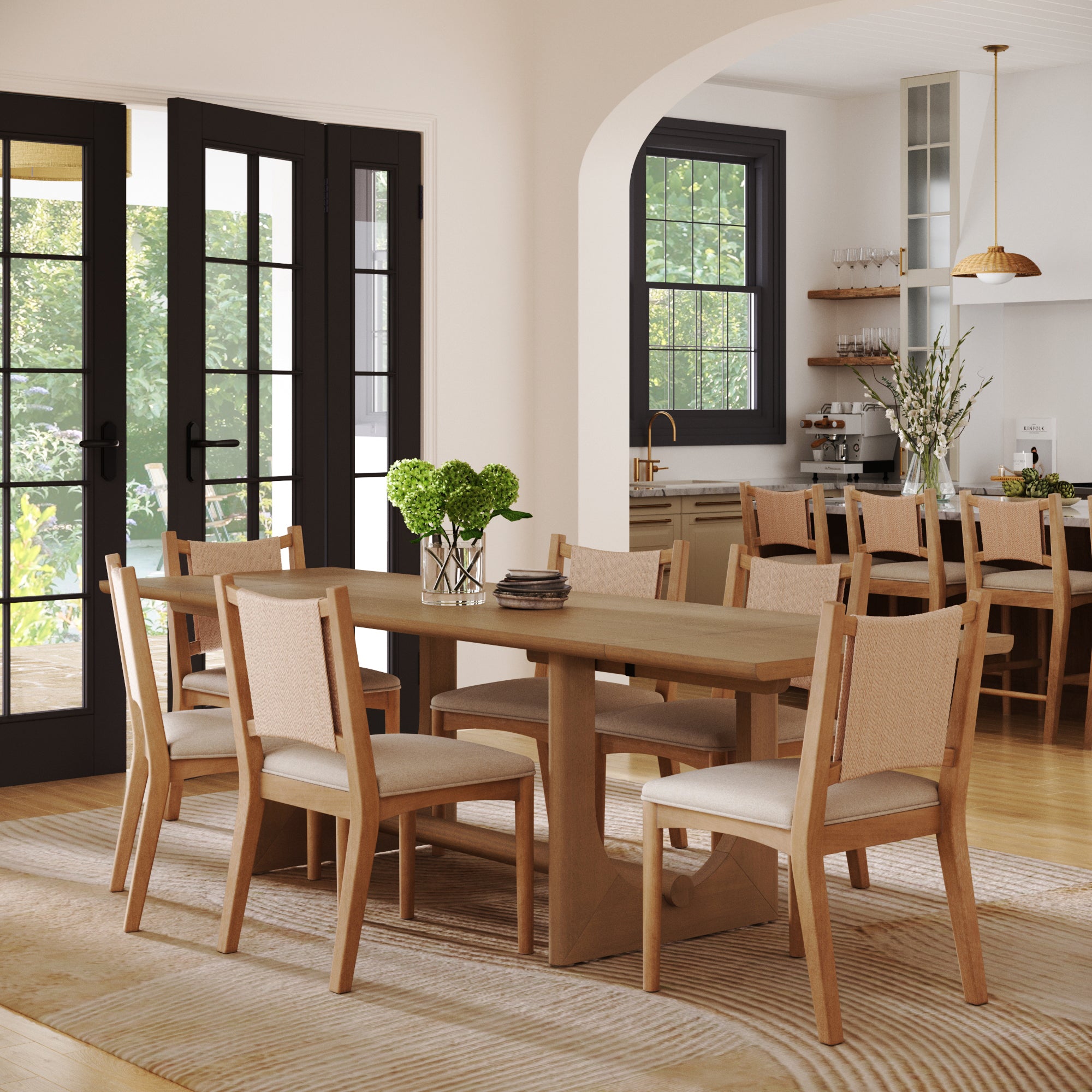 A bright dining room showcases the Nathan James Extendable Dining Table Set with 6 upholstered chairs, potted plants as centerpieces, a striped rug, and glass doors leading to a sunny outdoor area.